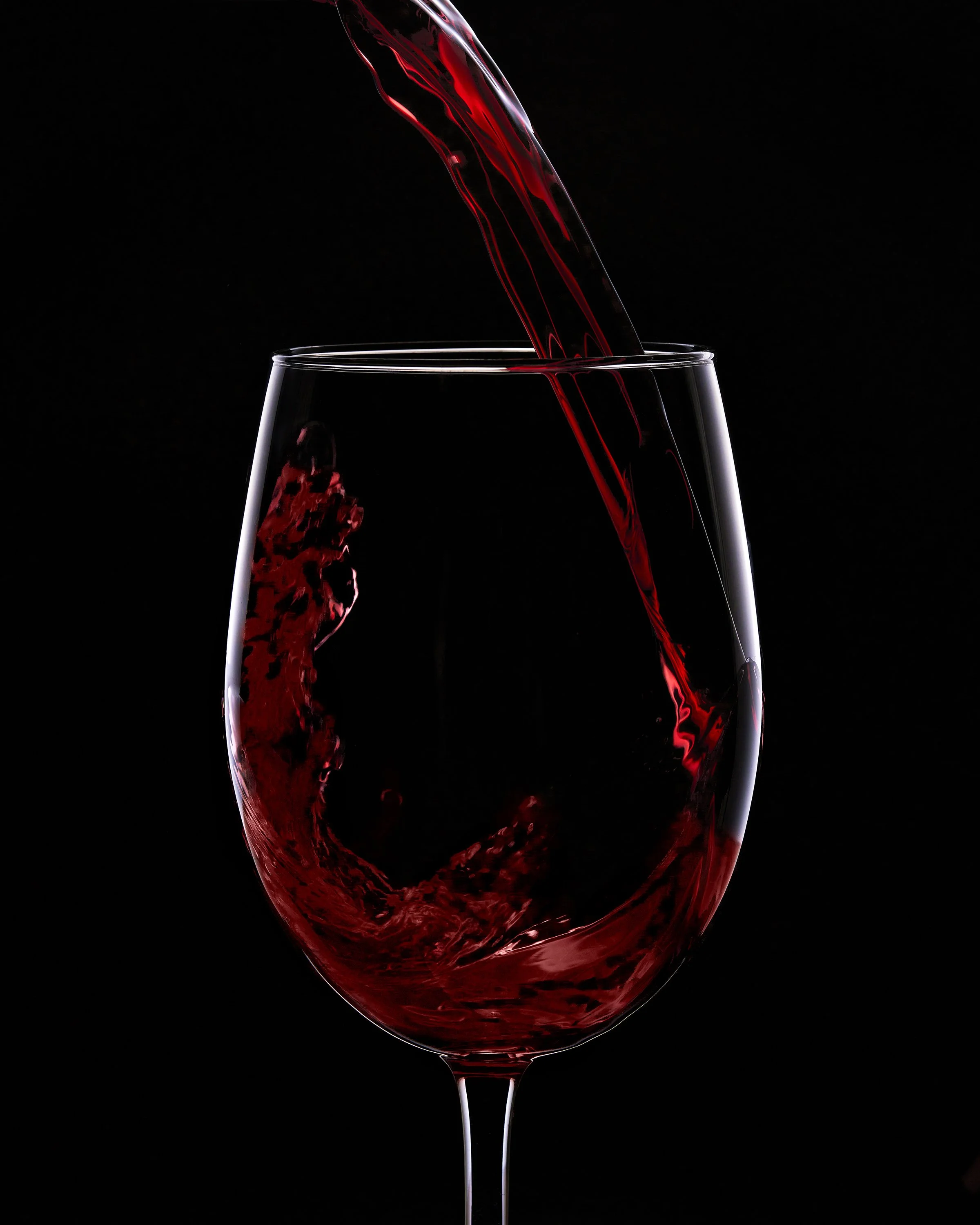 Red wine being poured into a clear wine glass against a black background.