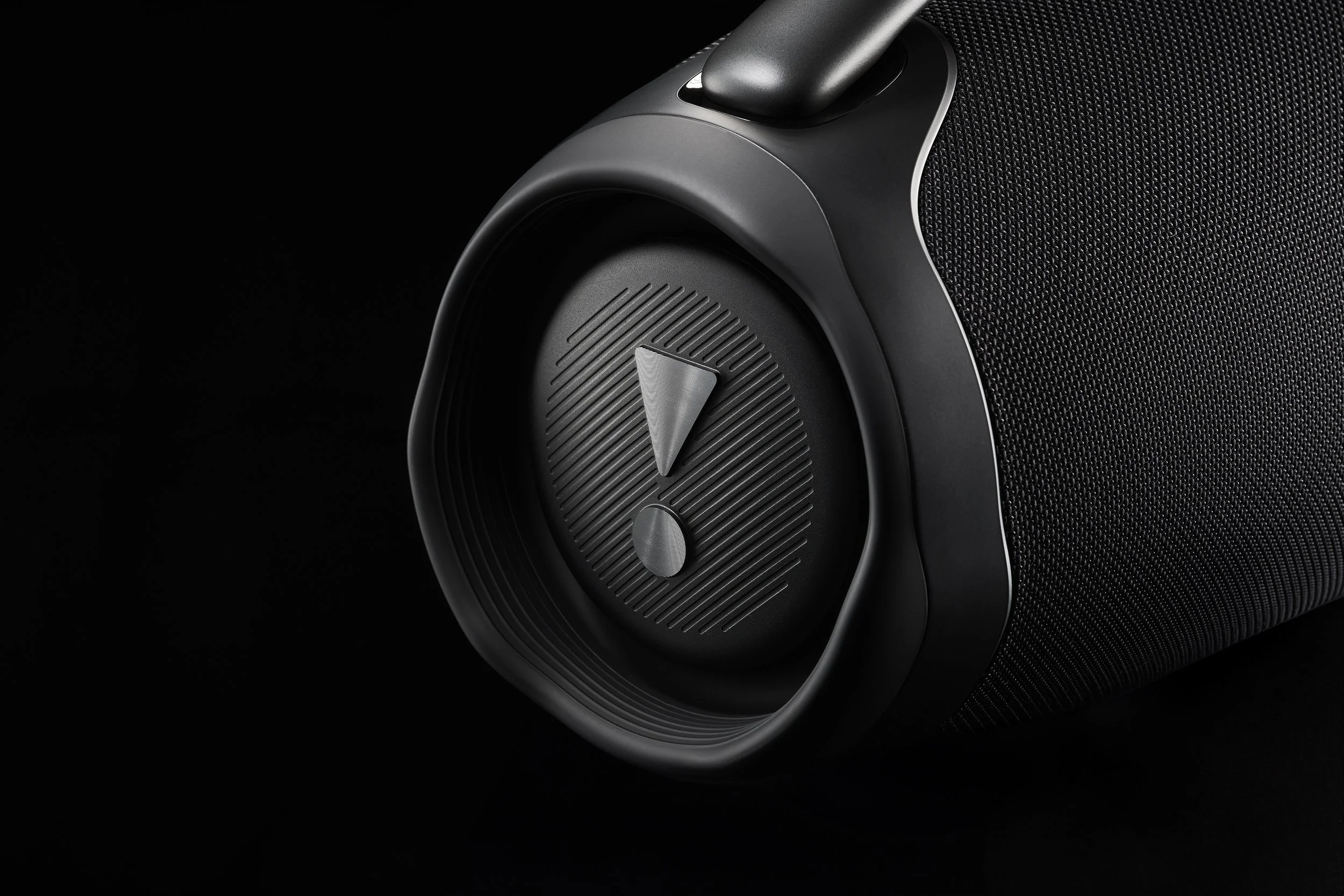 Close-up of a black portable speaker with a circular speaker grille and control knob, against a black background.