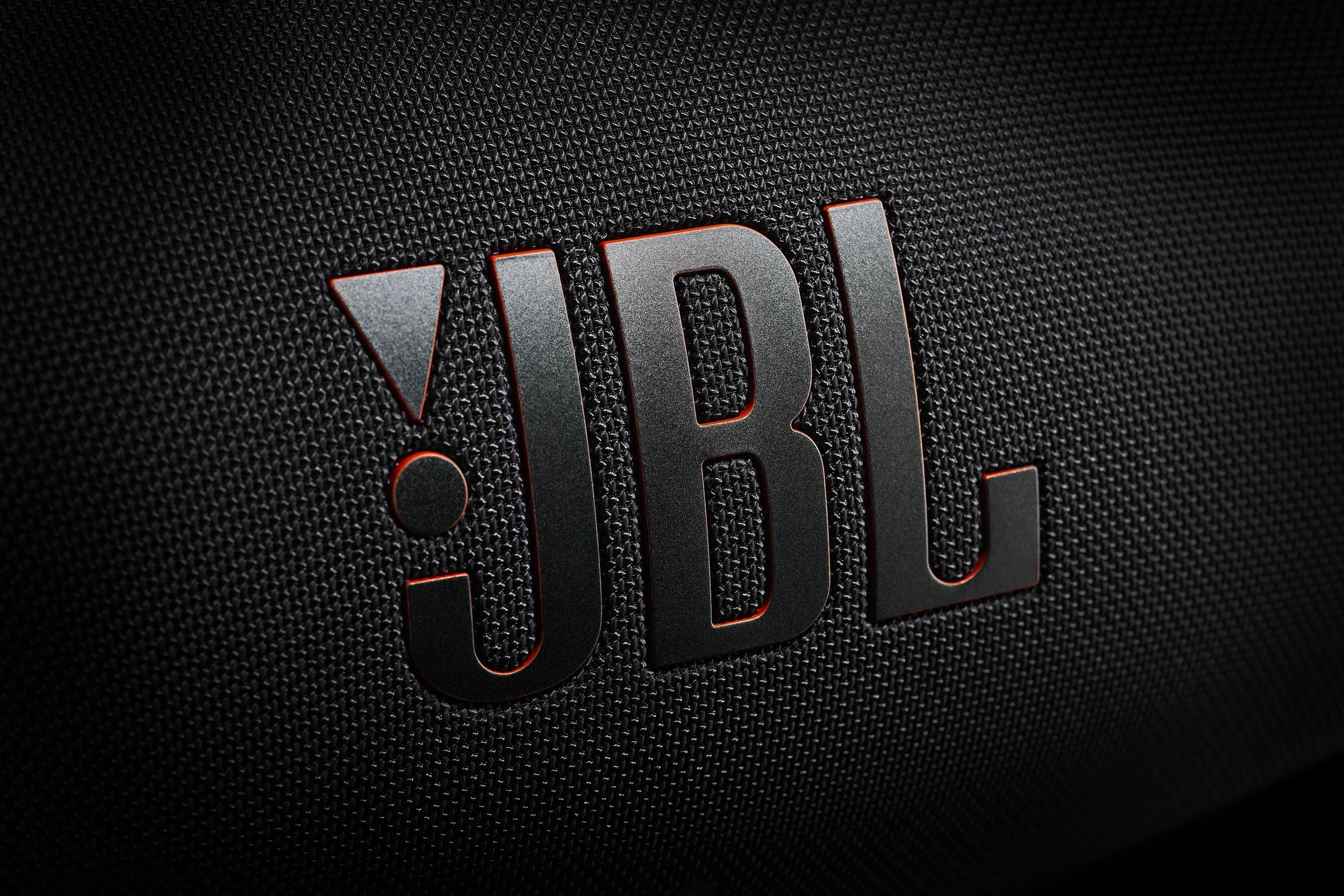 Close-up of JBL logo on a textured black speaker surface.