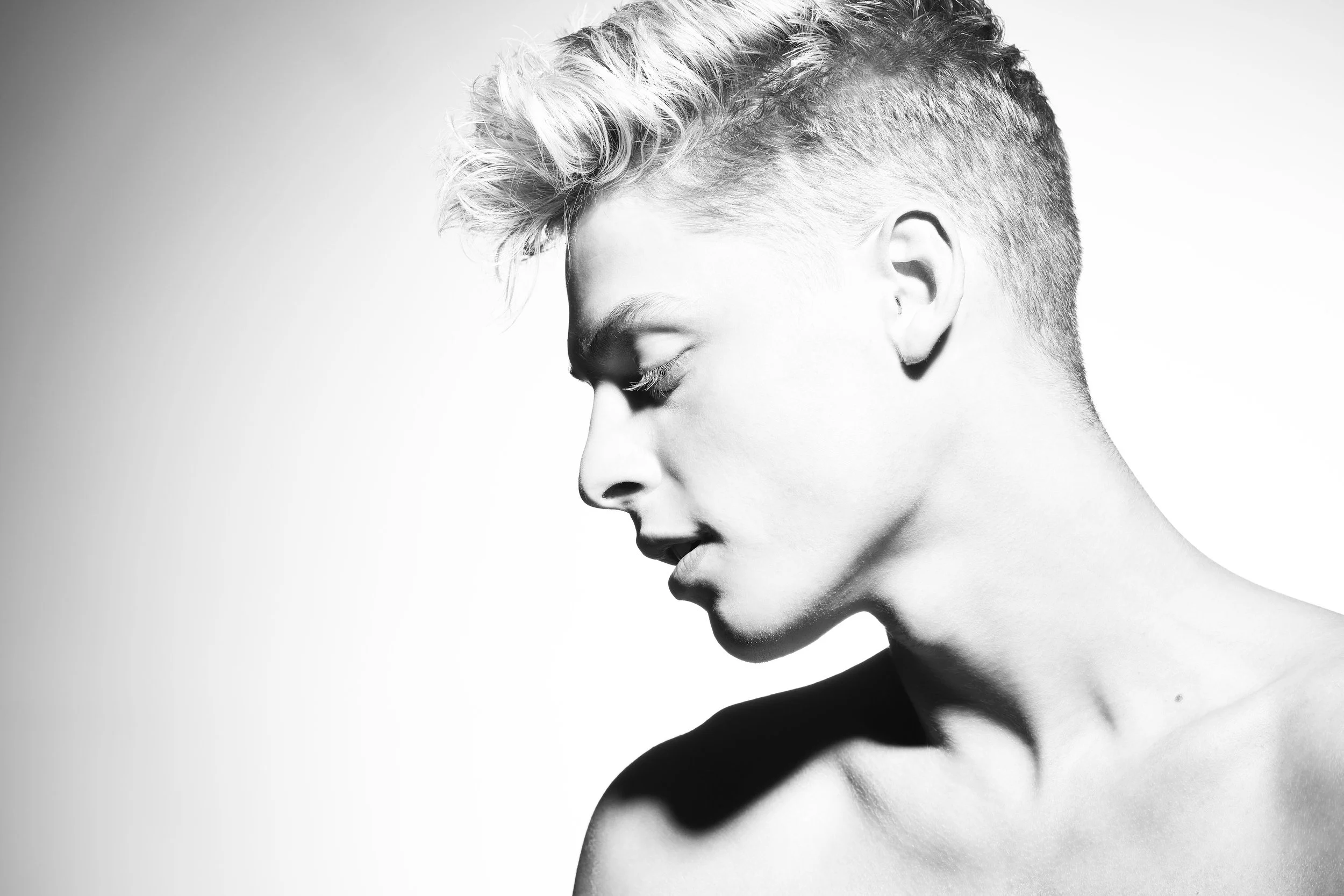 Black and white portrait of a young woman with short, textured hair, looking downward with eyes closed, shown from the shoulders up.