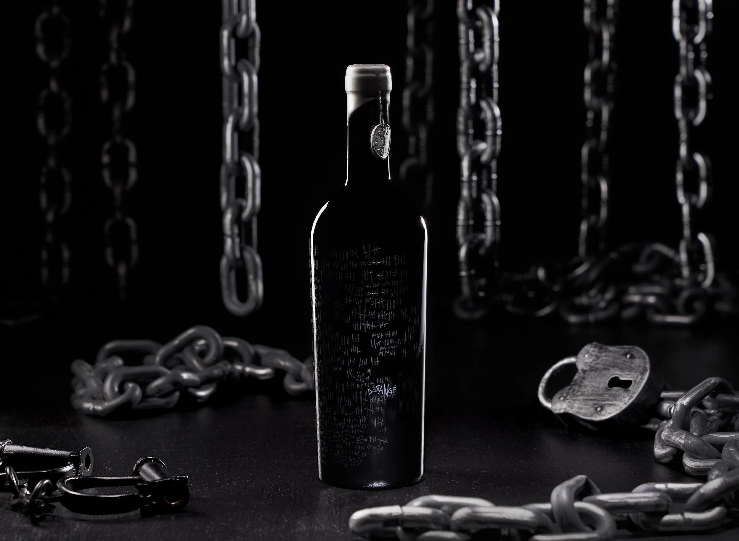 A black spray bottle centered among scattered metal chains on a dark surface with a dark background.