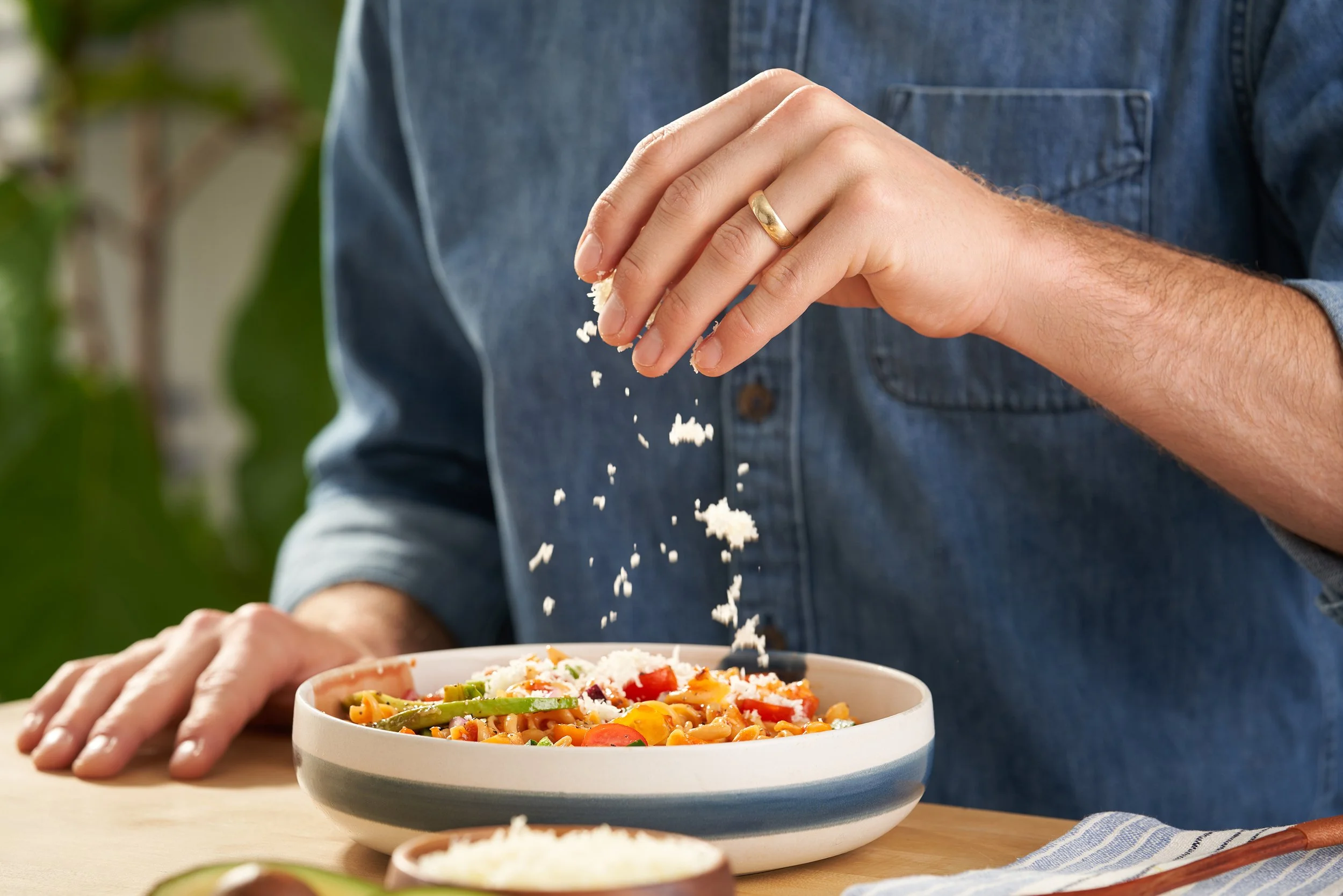 Person sprinkling cheese onto a bowl of pasta with vegetables.