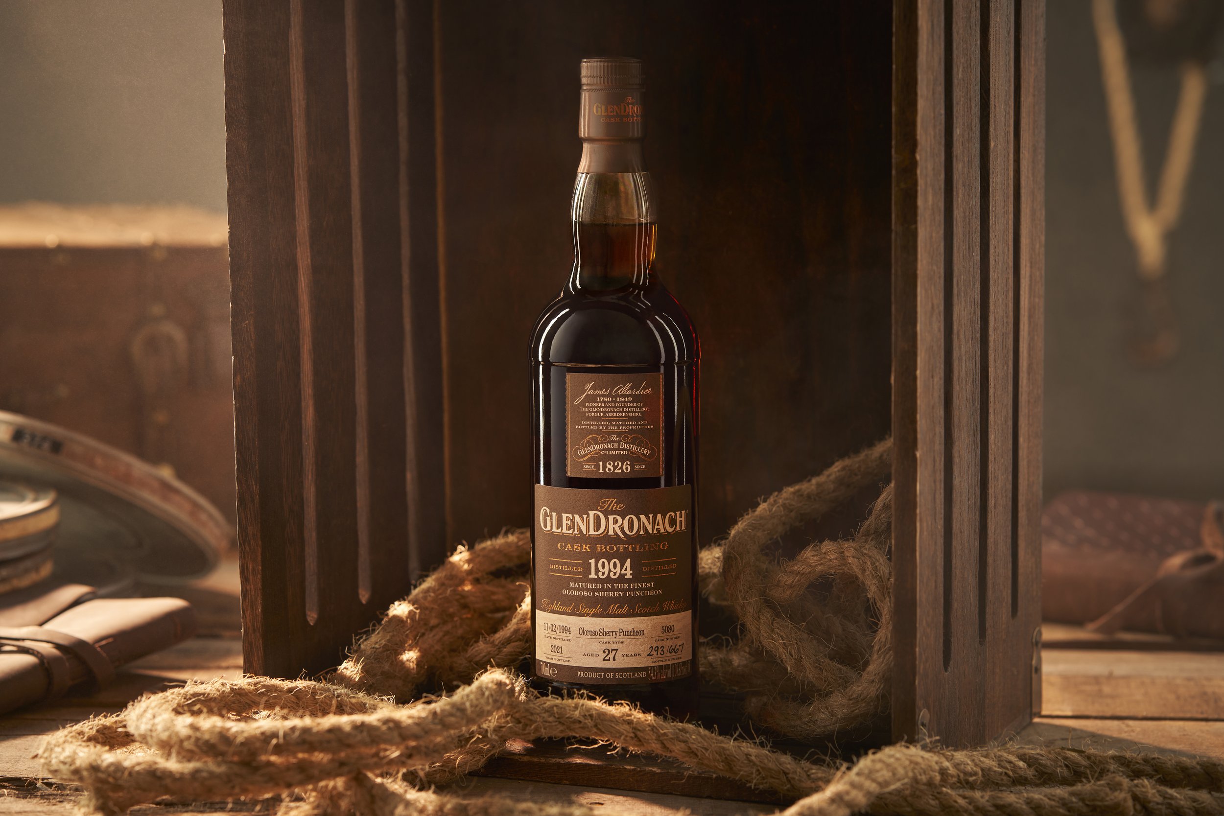 A bottle of GlenDronach single malt Scotch whiskey inside a wooden case, surrounded by thick ropes, on a wooden surface.
