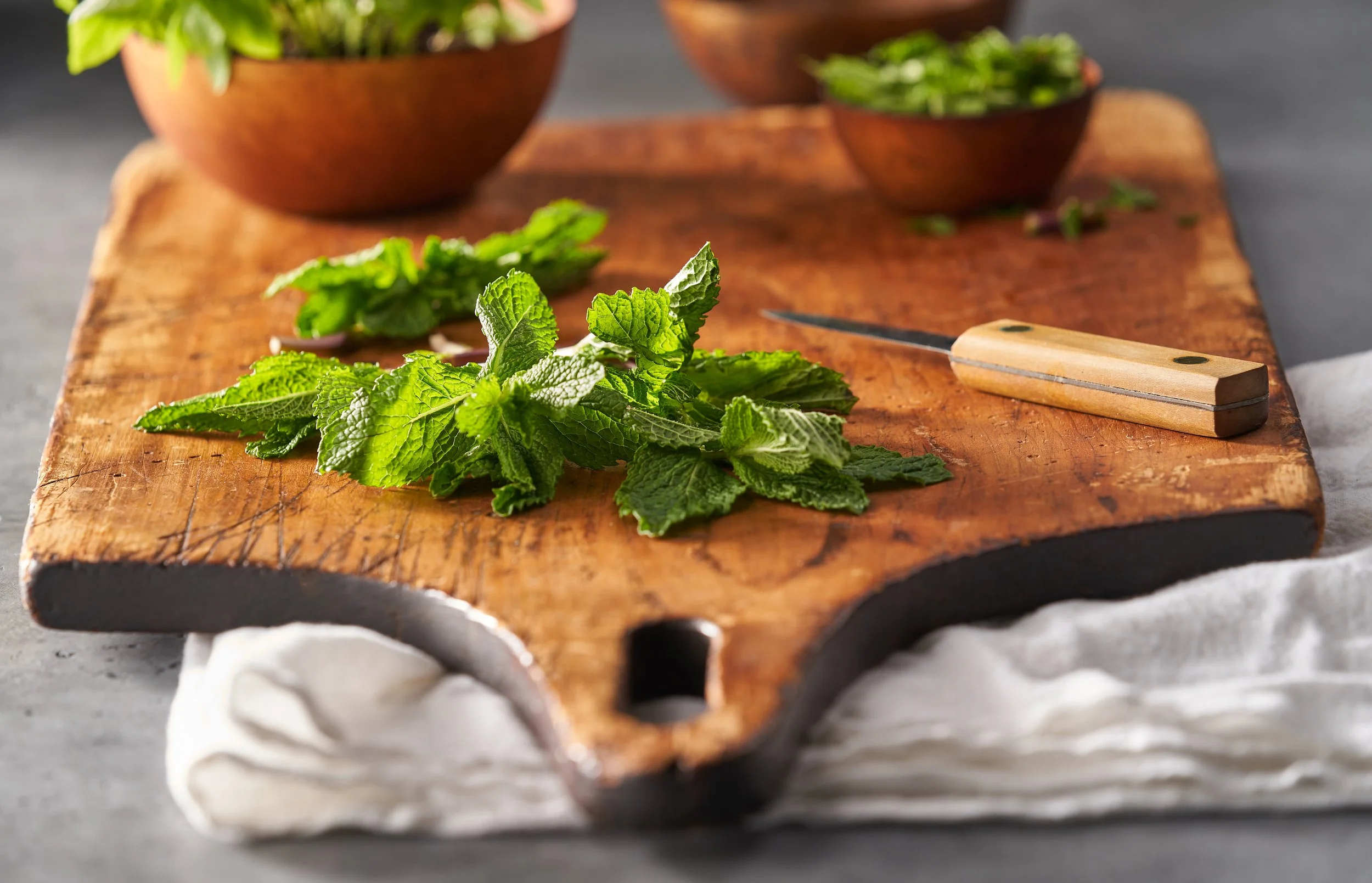 Fresh mint and herbs on a wooden cutting board with a small knife, in a kitchen setting.