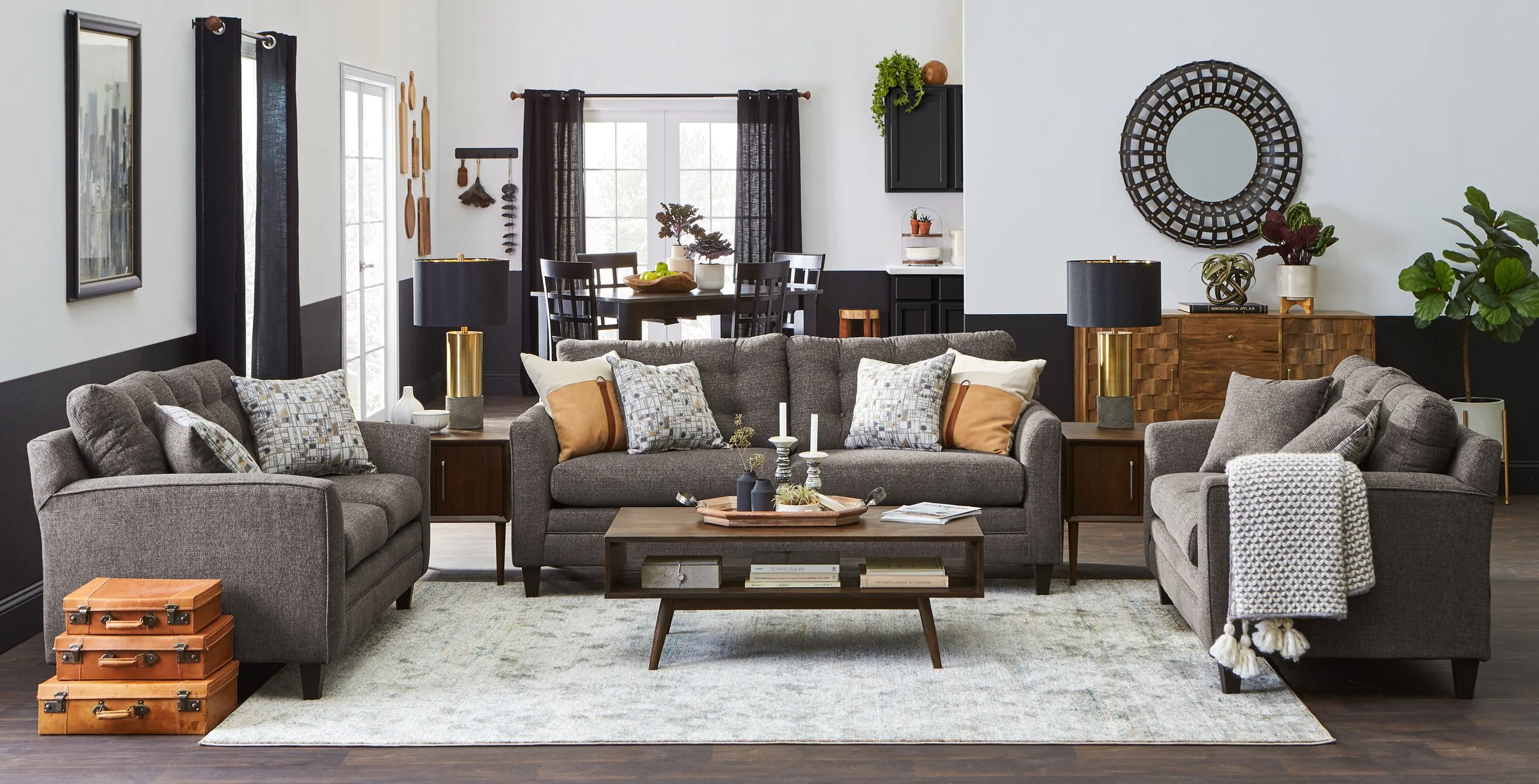 A living room with three gray sofas, a wooden coffee table, a beige rug, and various decor including lamps, plants, and wall art.