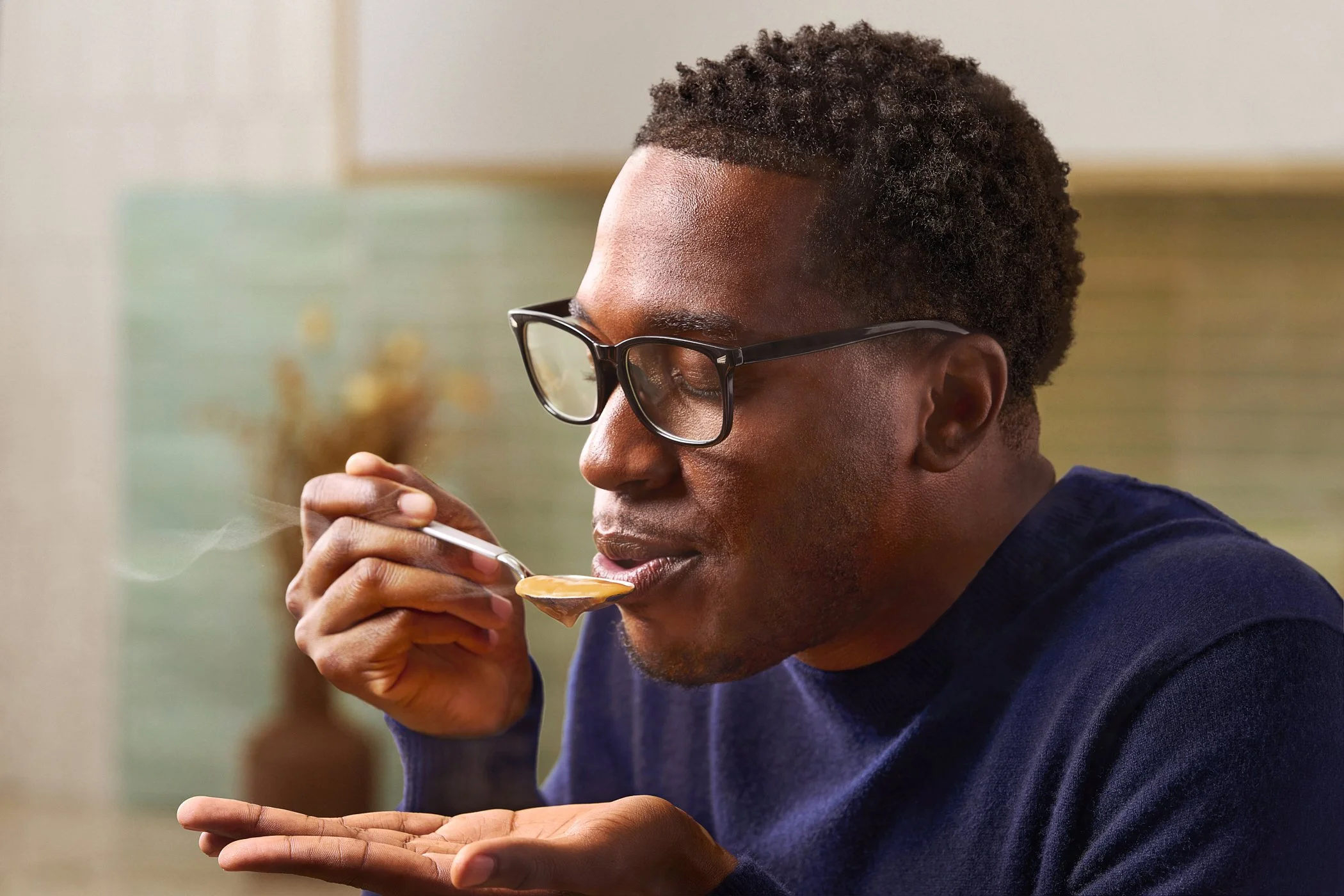 A man with glasses eating soup with a spoon.