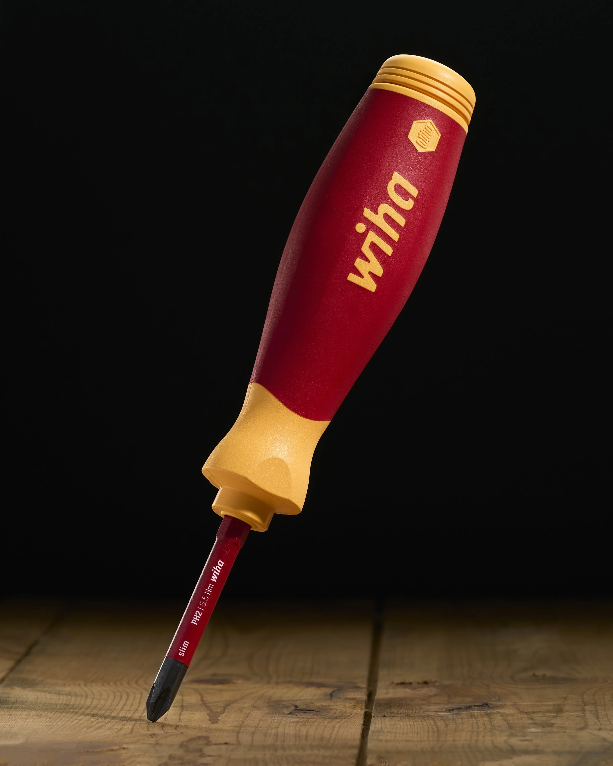 A red and yellow screw driver labeled 'Winda' resting on a wooden surface against a black background.