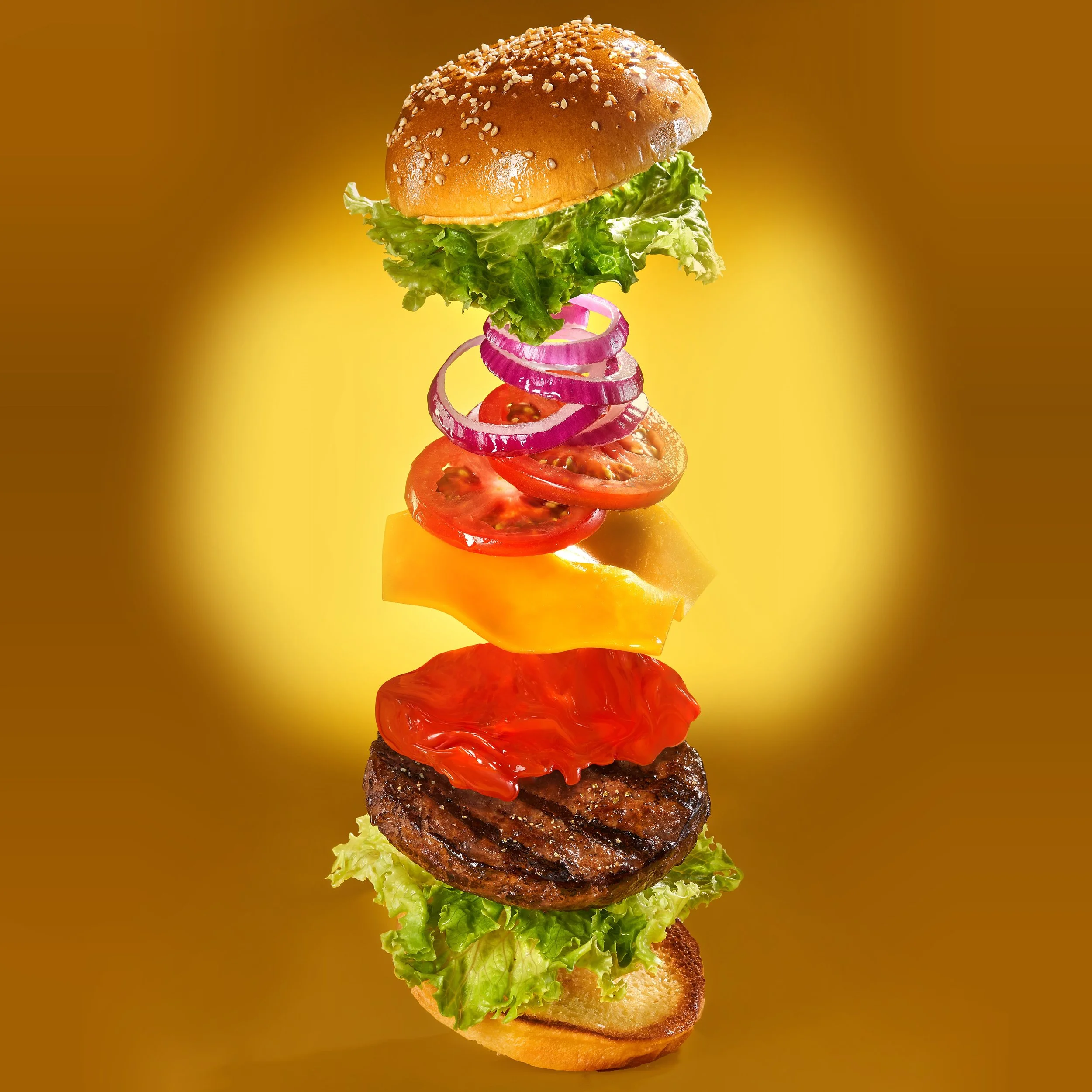 A deconstructed hamburger with layers of lettuce, grilled burger patty, sliced tomato, shredded cheese, red pepper, sliced onions, cherry tomatoes, and a hamburger bun with sesame seeds on top, all floating against a yellow background.
