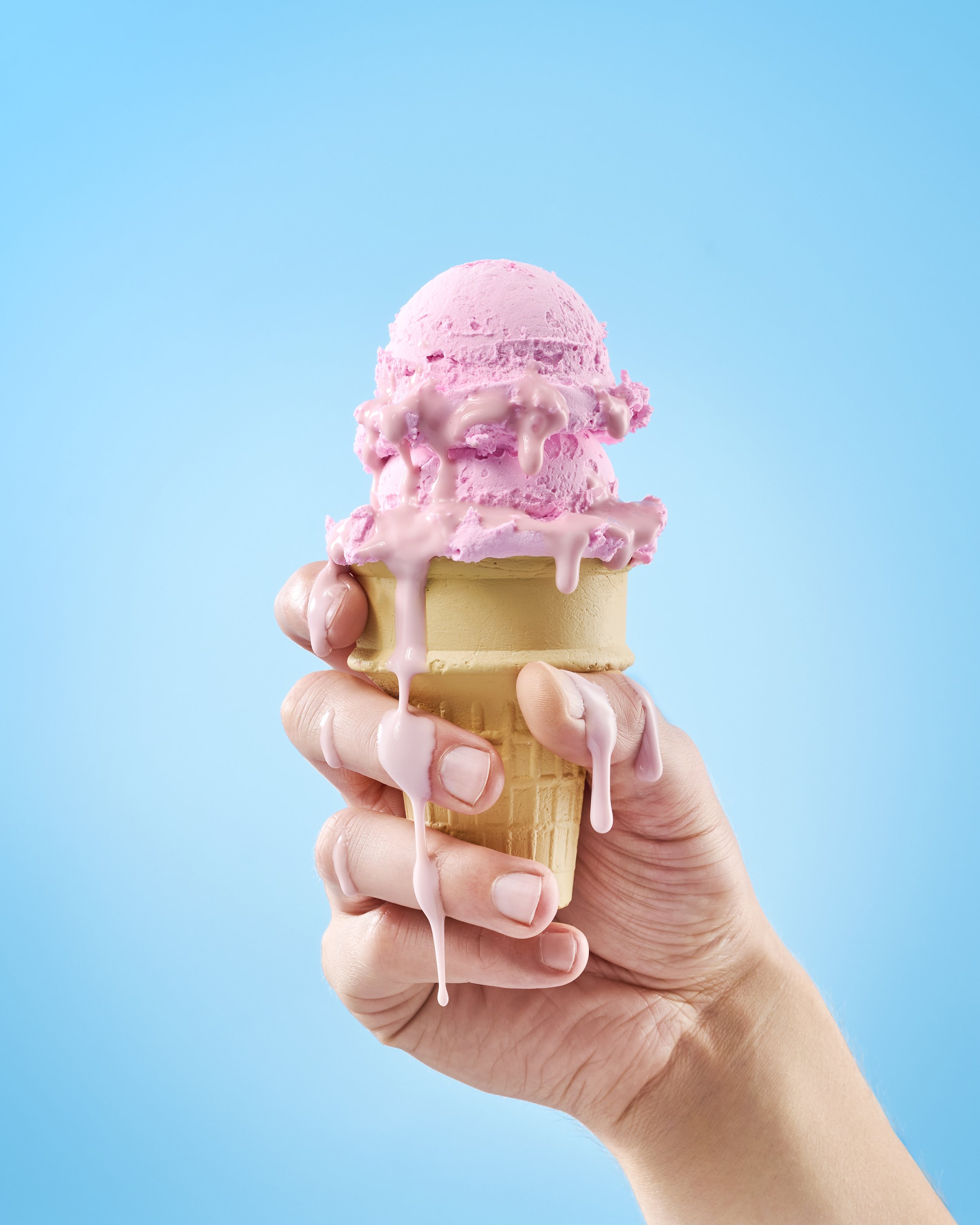 A hand holding a cone with pink ice cream on a blue background.