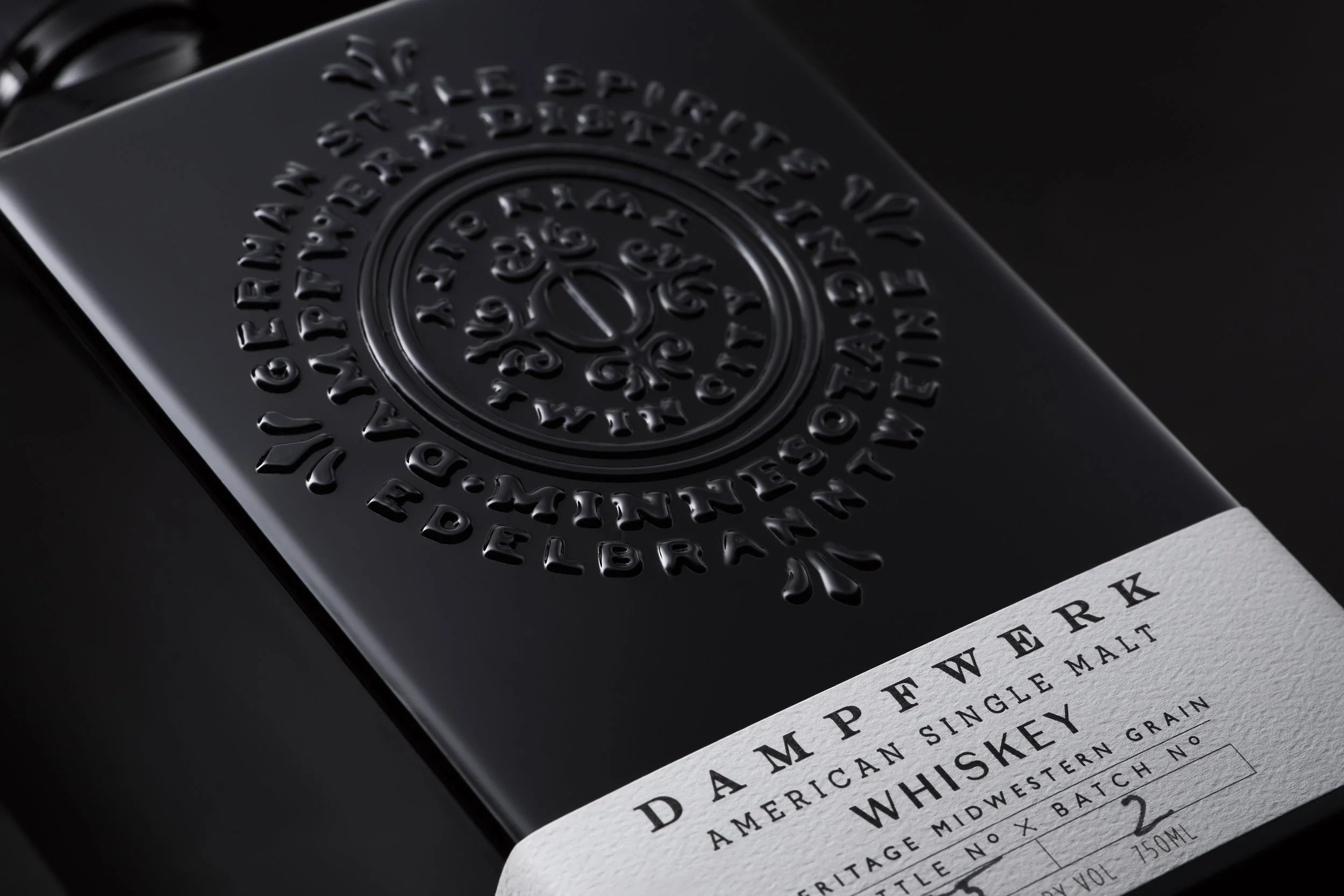 Close-up of a black bottle of Dampewerk American Single Malt Whiskey, with embossed logo and a white label showing the brand name and whiskey details.
