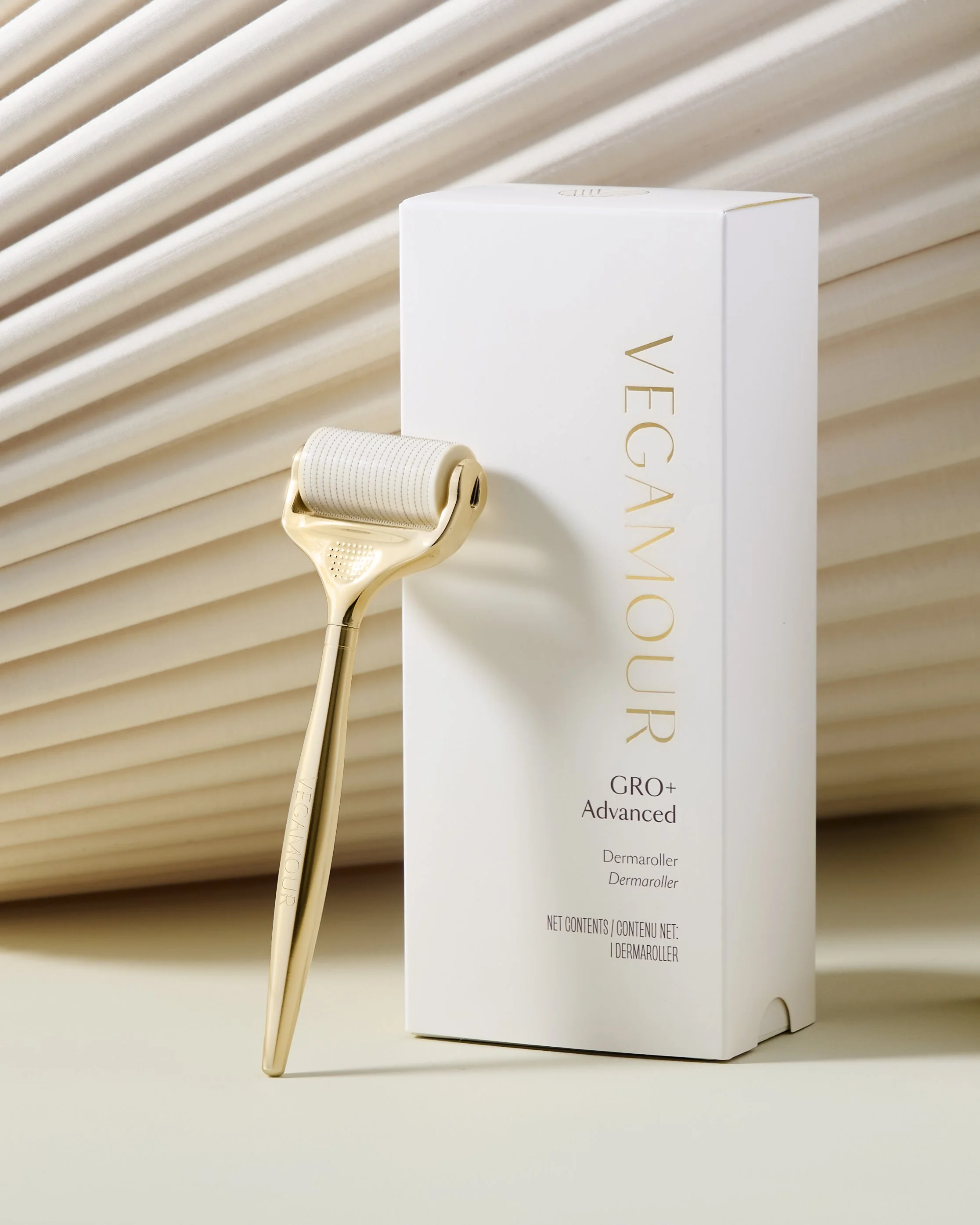 Gold dermaroller with white handle leaning against a white box labeled VEGA MOUR with gold and black text