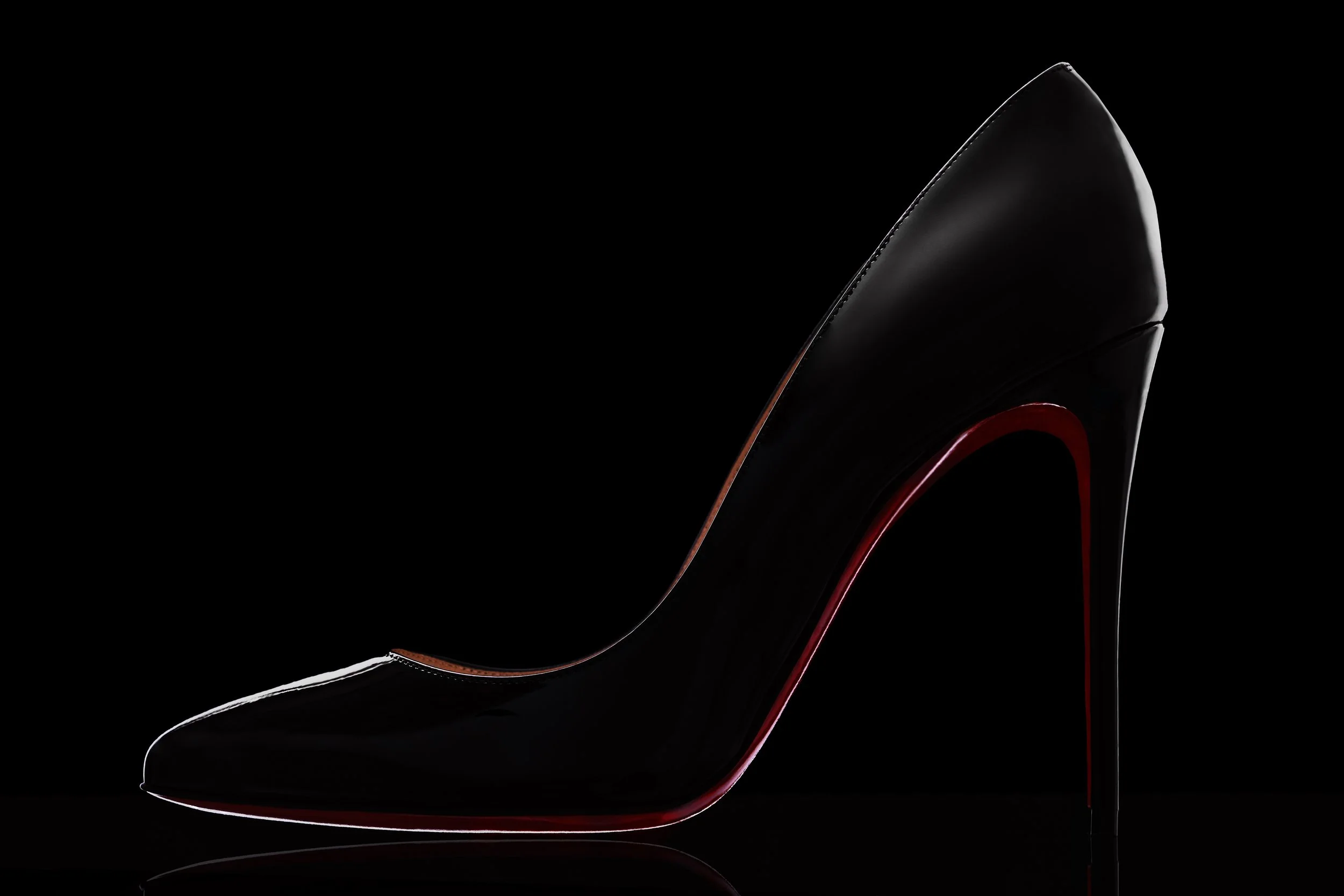 Close-up of a black high heel shoe with red accents, set against a dark background.