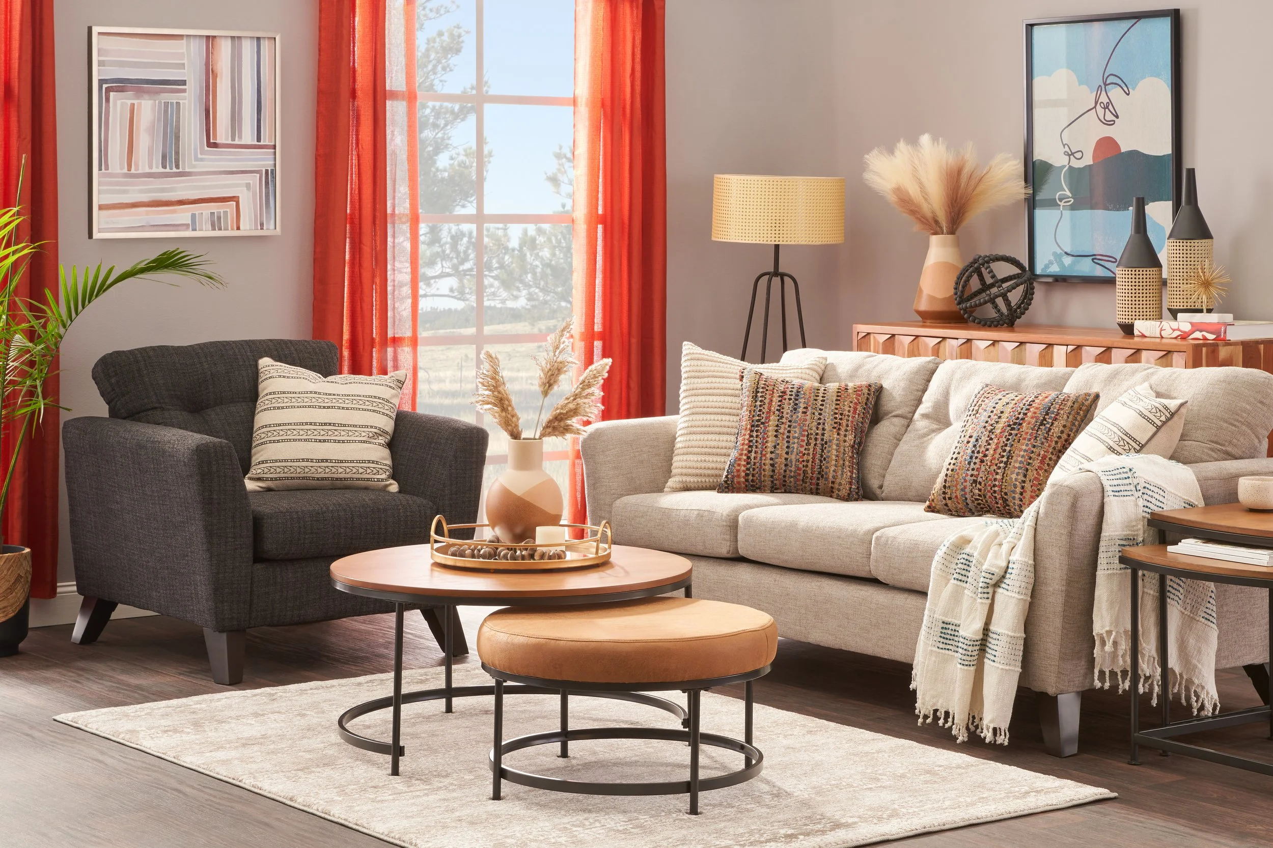 Living room with beige couch, black armchair, round coffee table, side table, floor lamp, artwork, potted plant, decorative vases, and window with red curtains