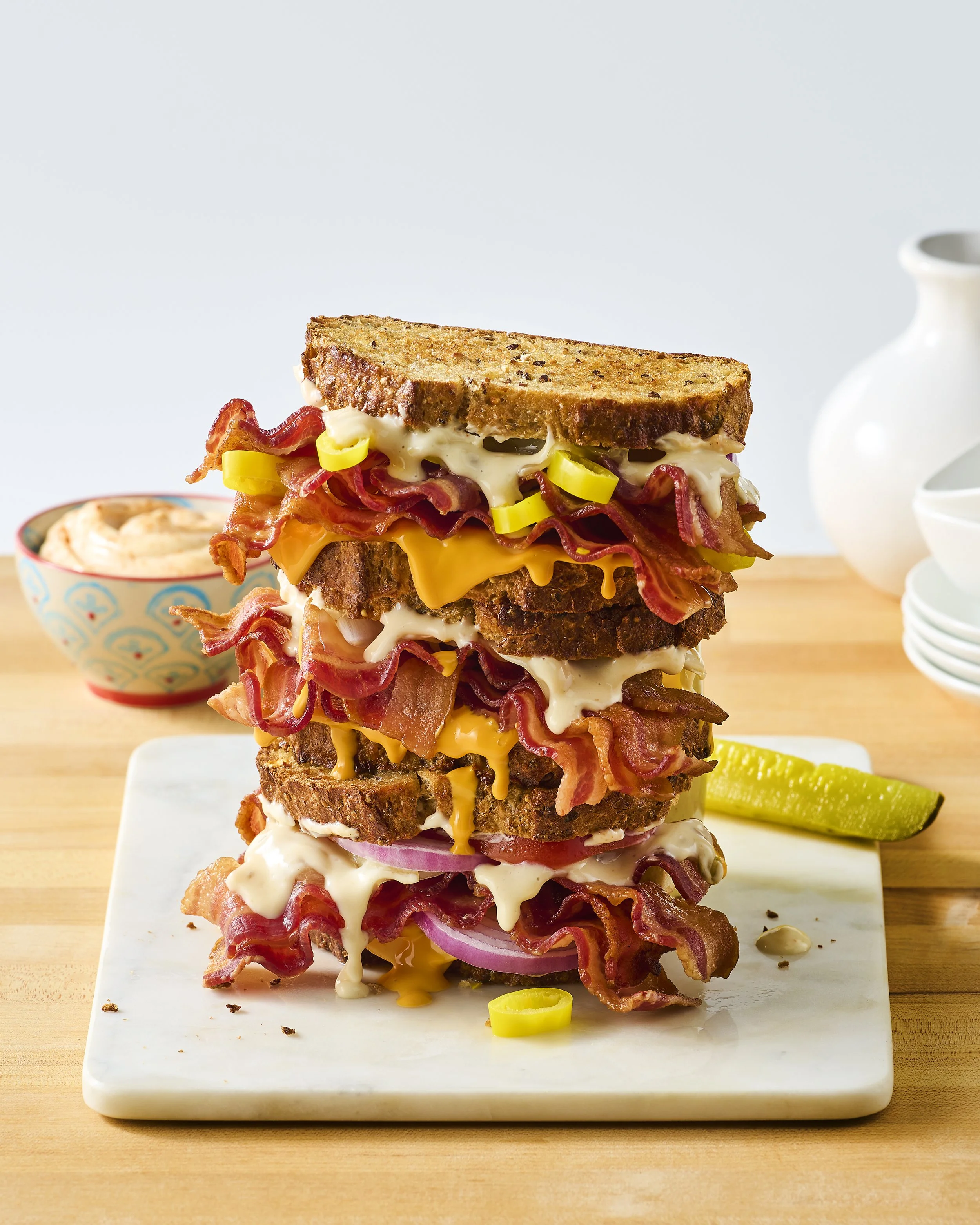 Tower of bacon, cheese, and sandwich bread with melted cheese, bacon, and green onions on a white marble cutting board.