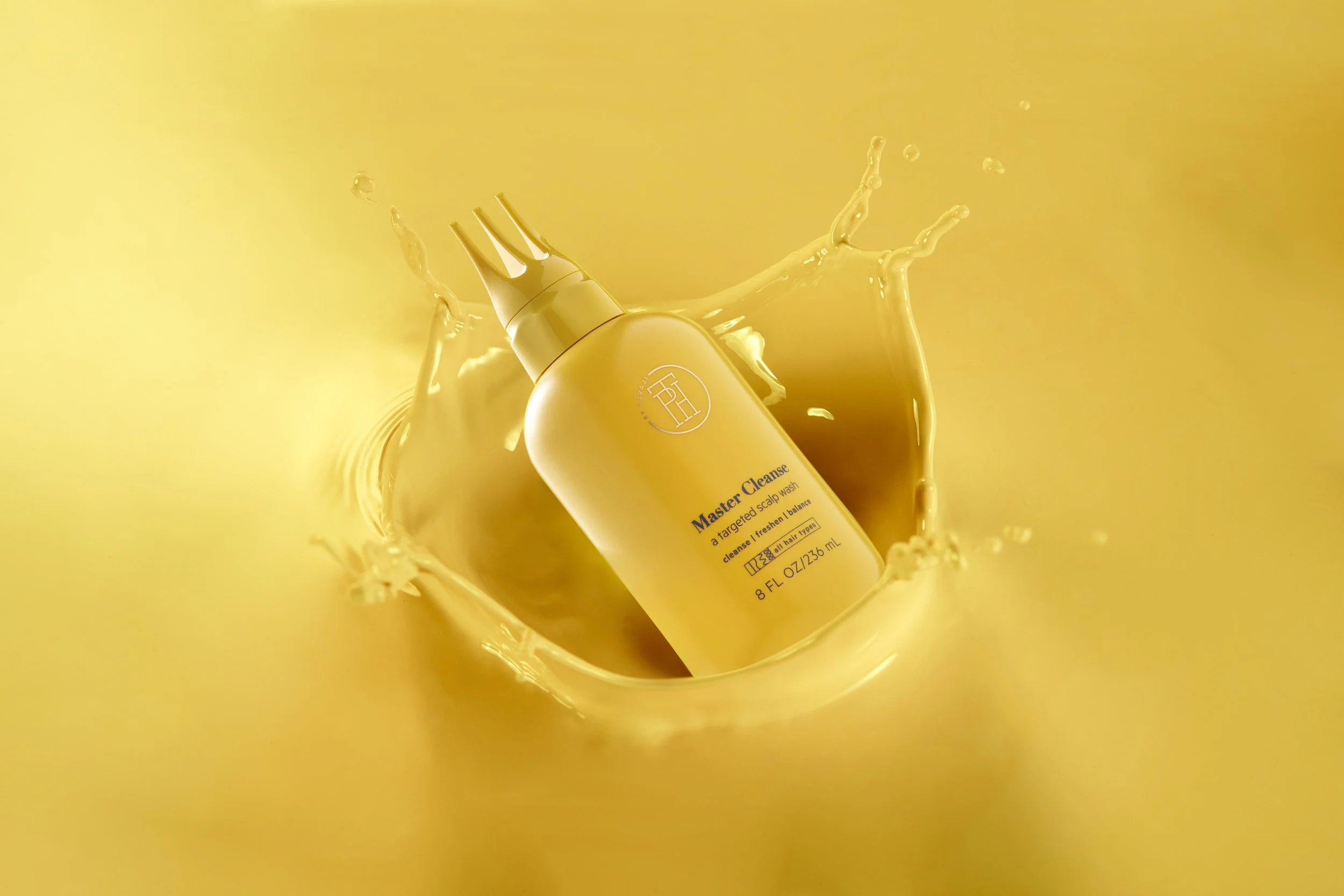 A yellow bottle of hair care product for scalp cleansing, labeled 'Master Cleanse,' submerged in a splash of matching yellow liquid against a yellow background.