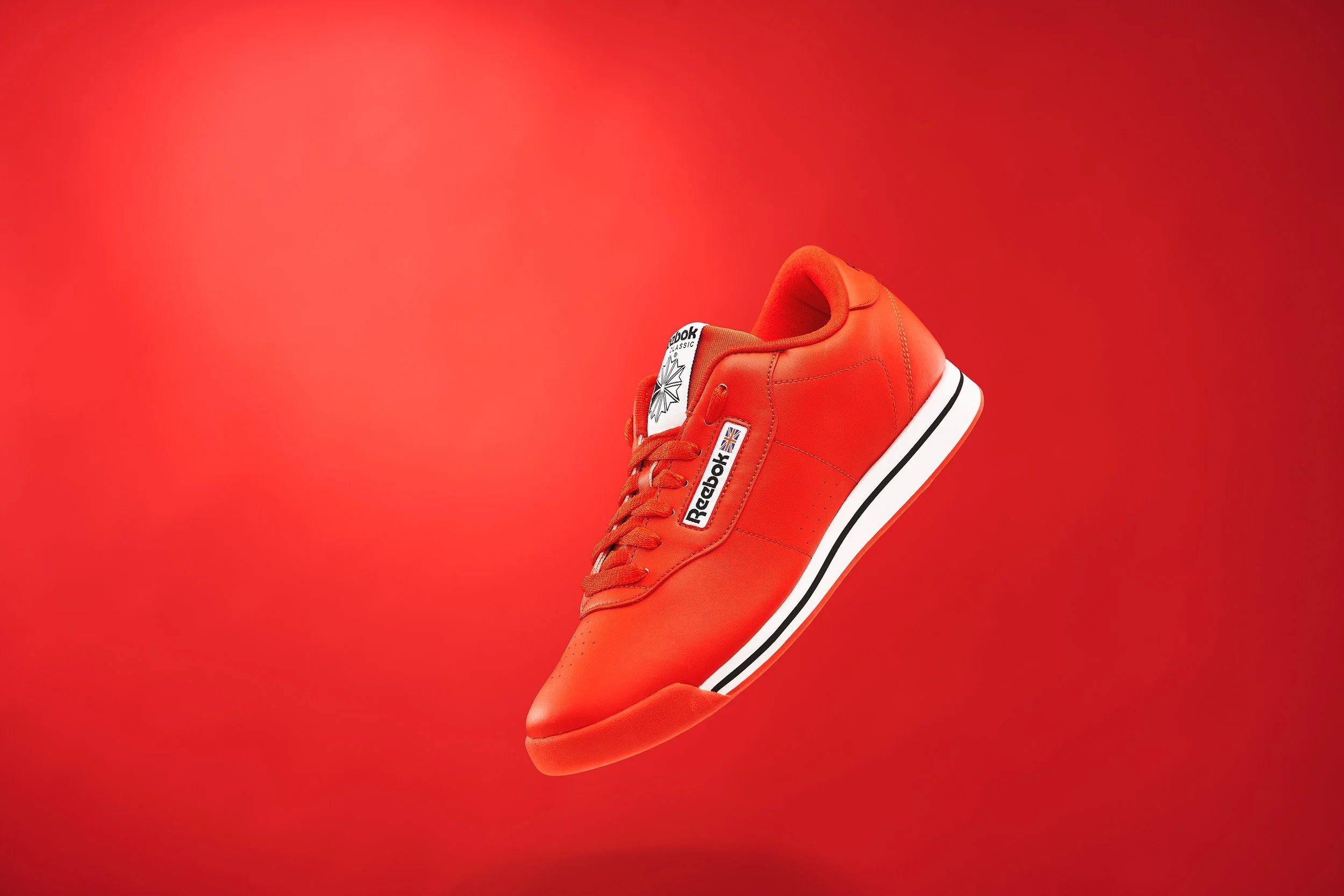 A red Reebok sneaker floating against a matching red background.