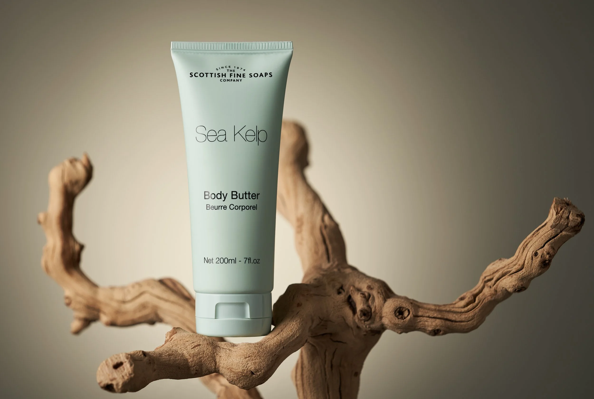 A tube of Scottish Fine Soaps Sea Kelp Body Butter balanced on a twisted piece of driftwood, with a plain background.