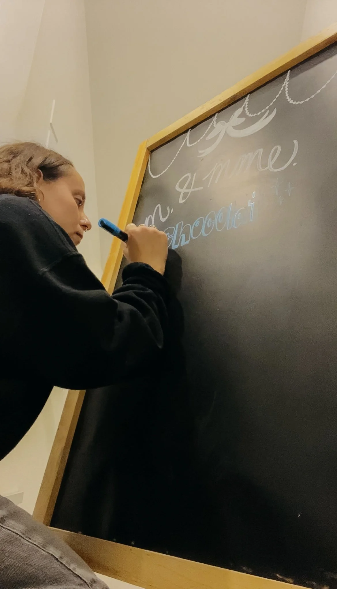 Une femme écrit sur un tableau noir avec un marqueur blanc et bleu.