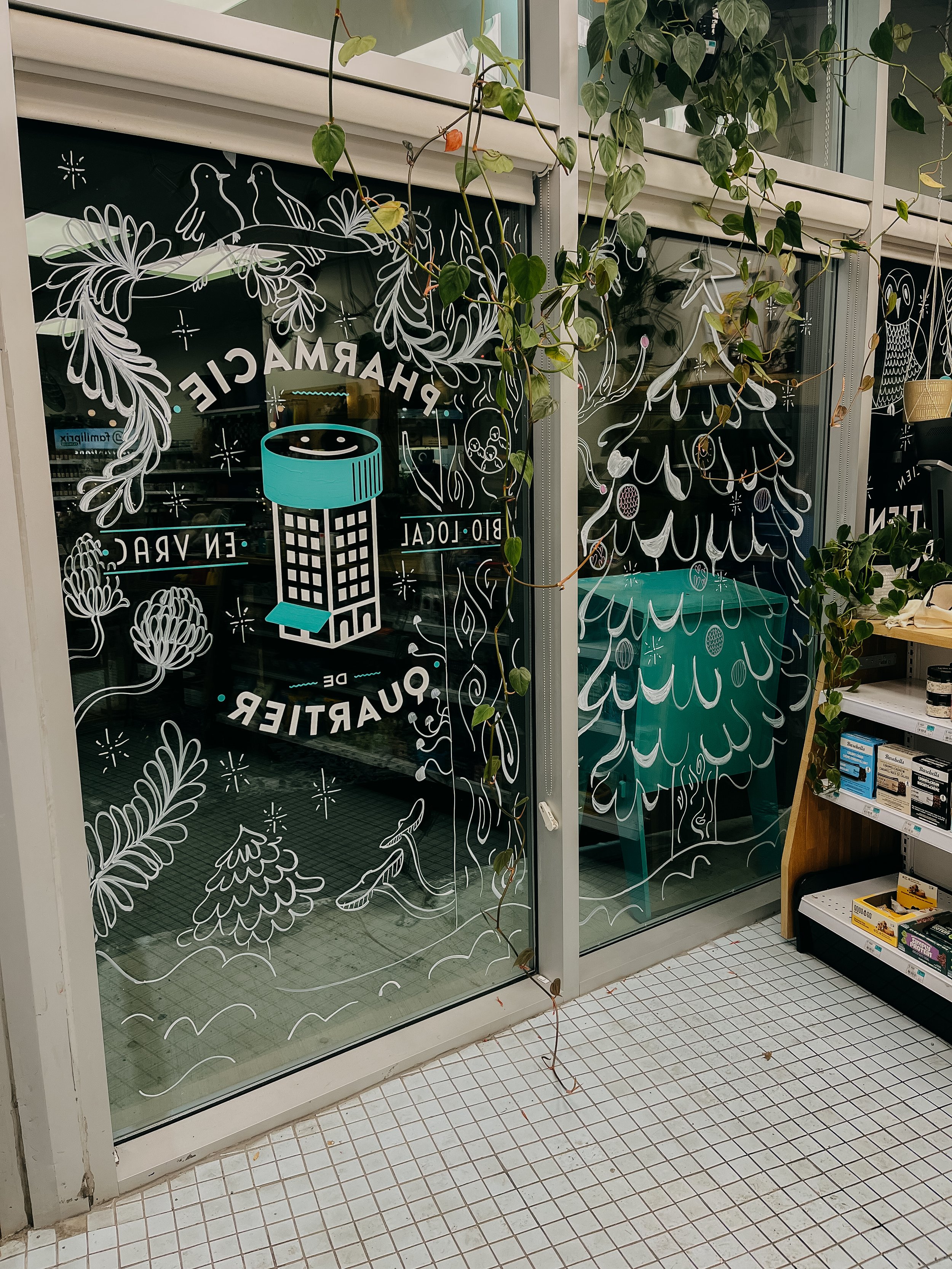Une porte en verre décorée avec des dessins blancs représentant des arbres, des oiseaux, une faune et un message publicitaire pour un bar-restaurant. Il y a également des plantes grimpantes accrochées à la fenêtre.