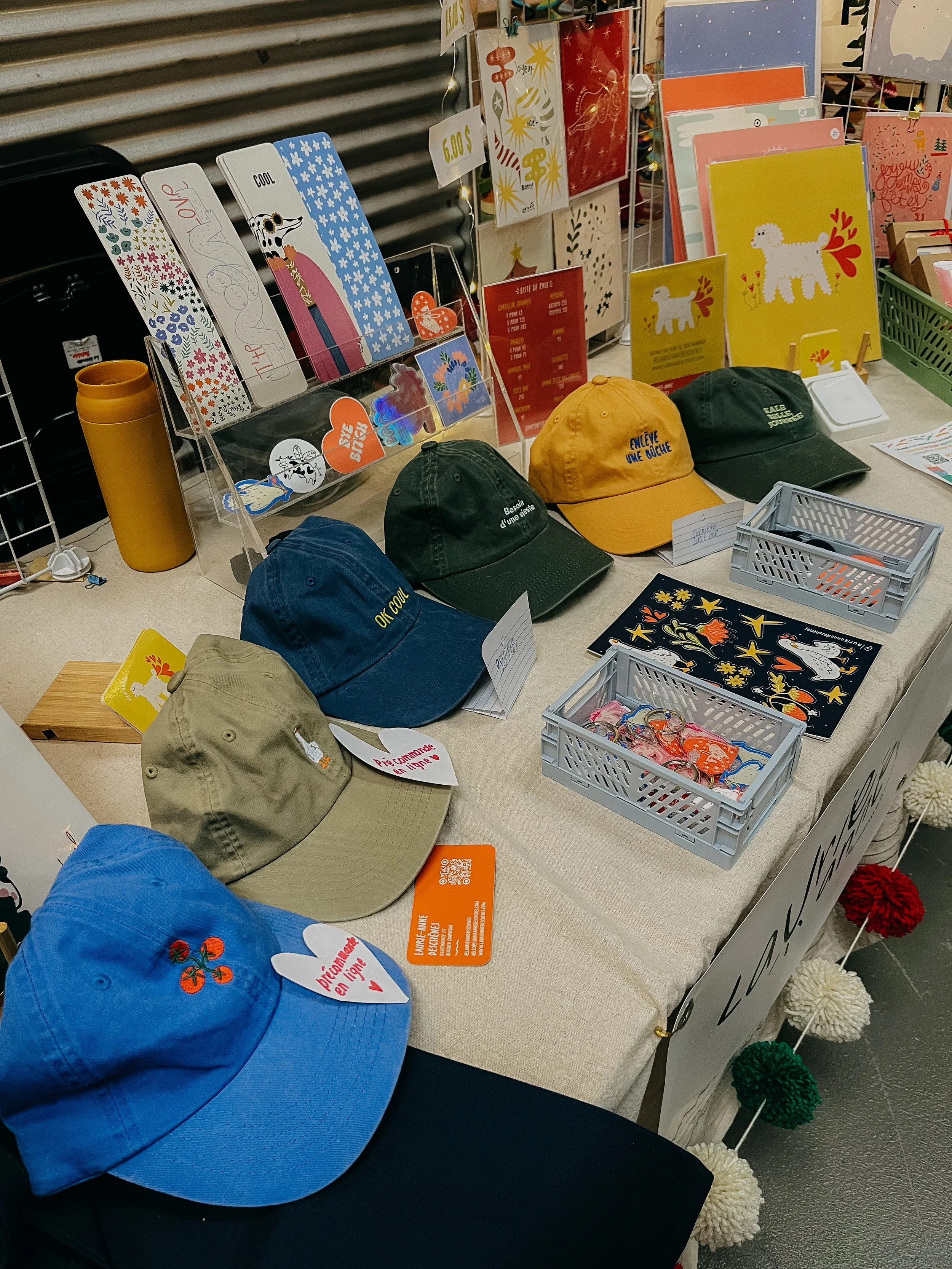 Table avec des casquettes de différentes couleurs, produits décoratifs et cartes cadeaux dans une boutique.