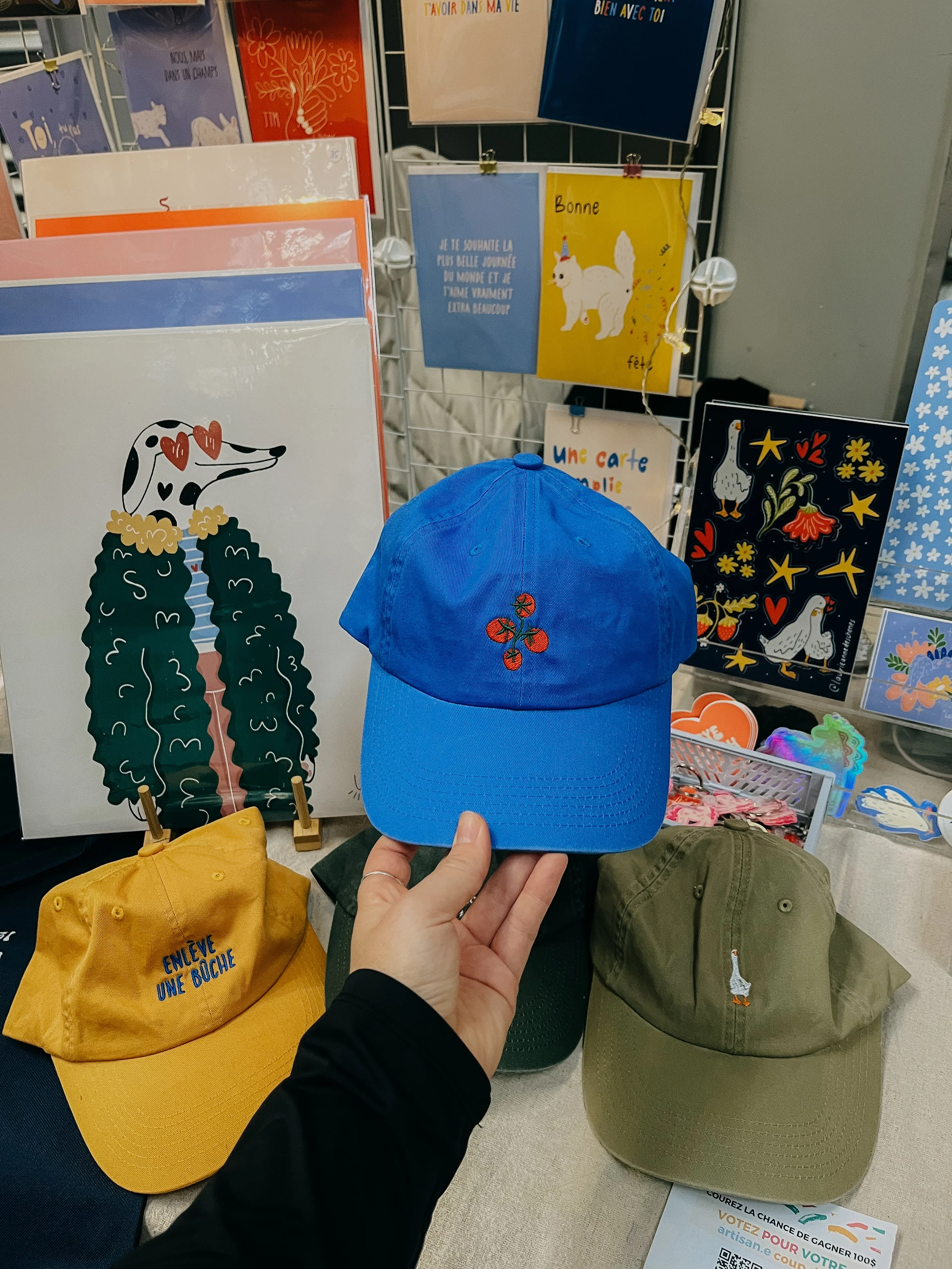 Casquettes colorées exposées, avec une casquette bleue au centre ornée de 3 cerises rouges, entourée par d'autres casquettes jaunes, vertes et kaki.