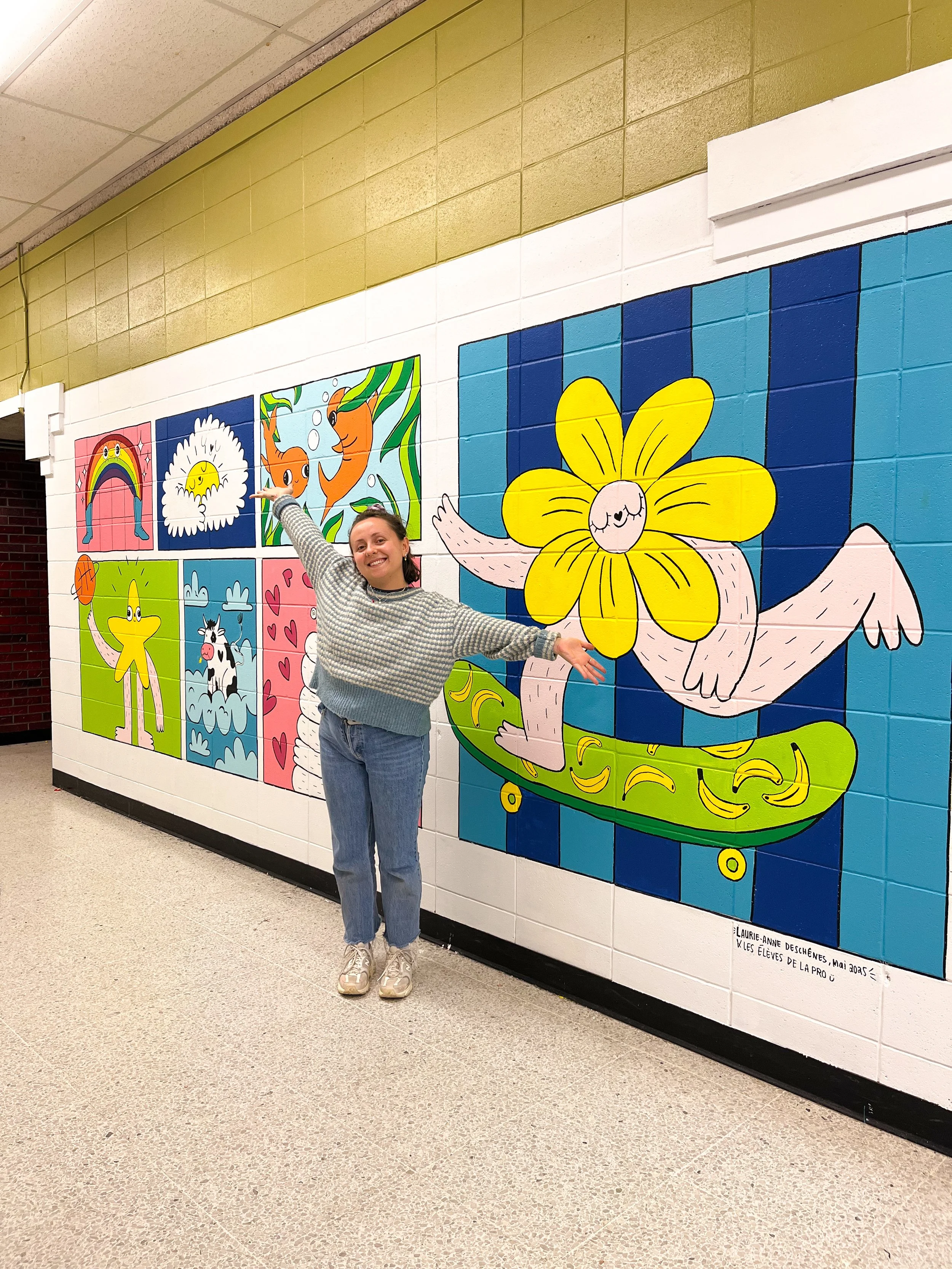 Femme souriante posant devant un mur peint avec des illustrations colorées de dessins animés d'animaux et de personnages fantastiques dans une école.