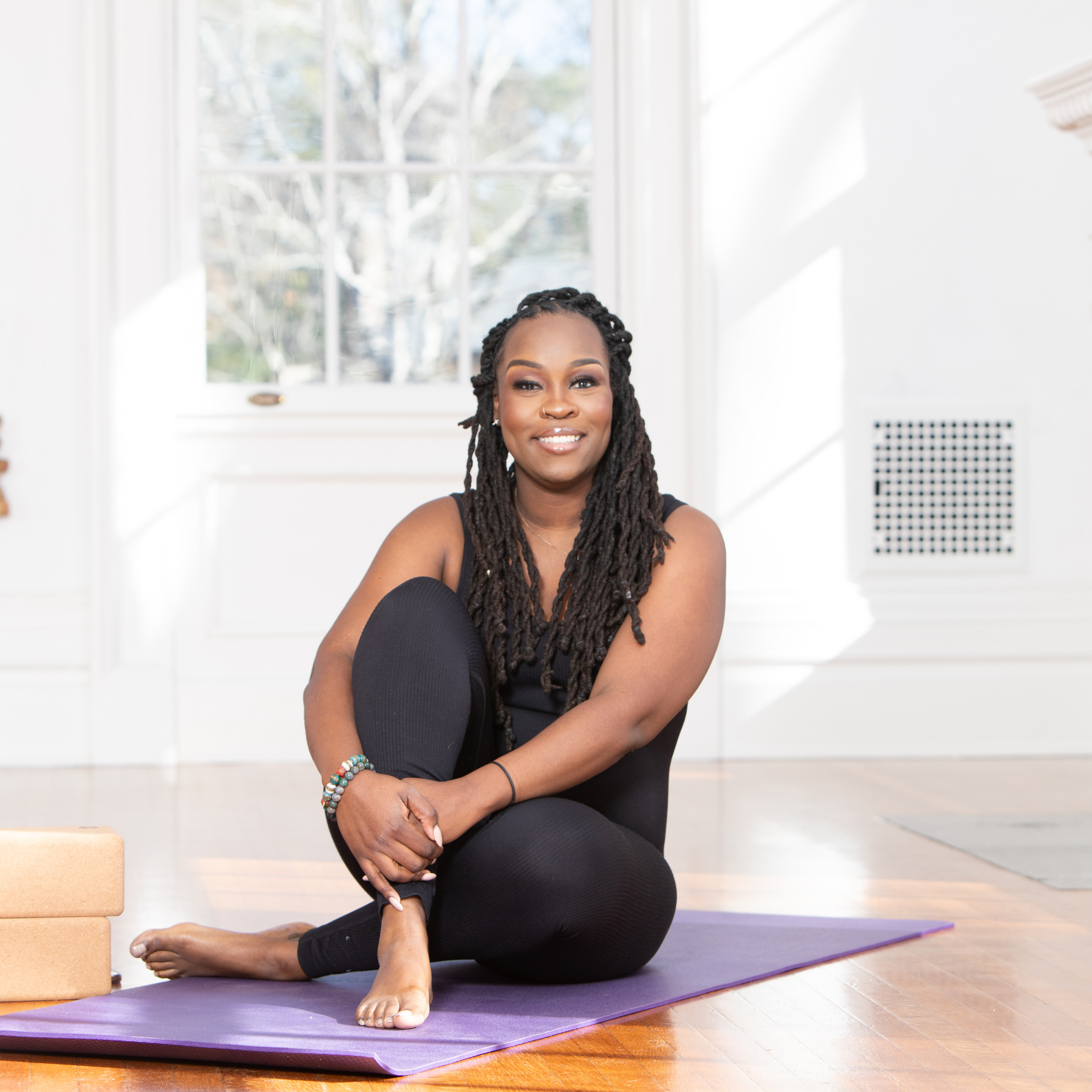 Woman practicing yoga on purple mat indoors near window