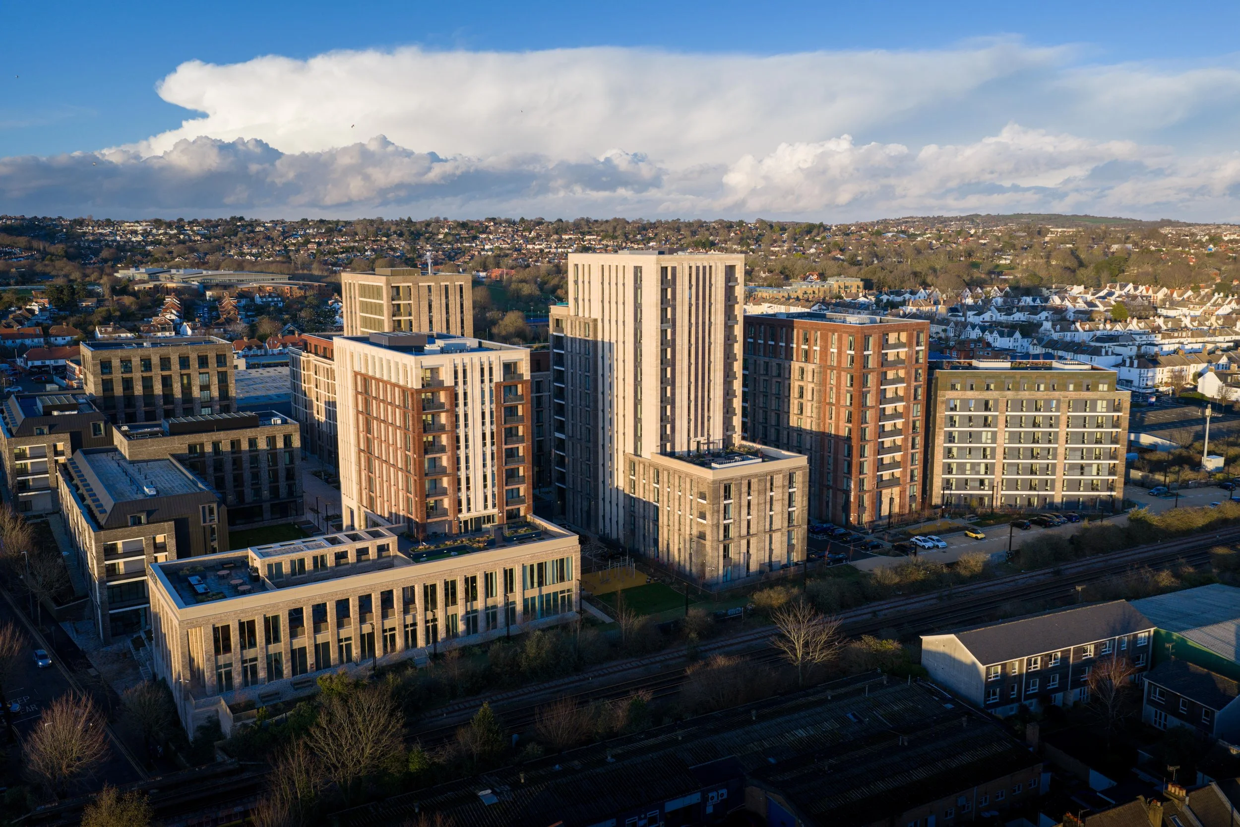 High-rise residential buildings in an urban area with a hillside in the background under a partly cloudy sky.