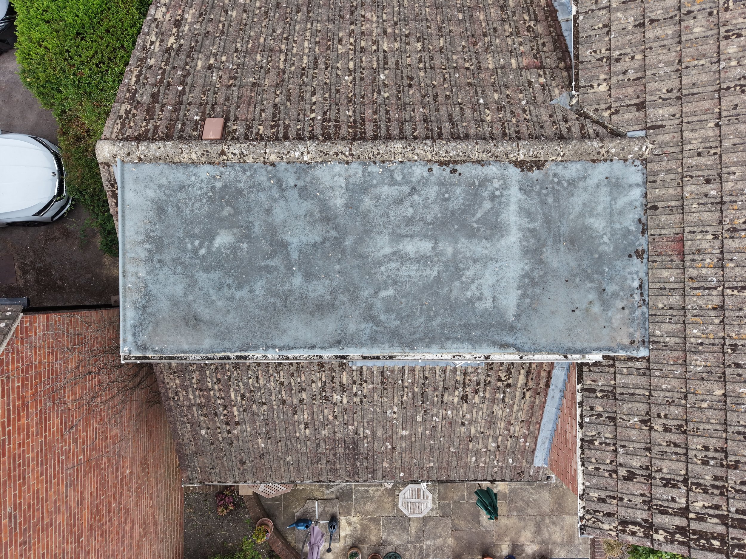 View of a rooftop with weathered bricks, a concrete section, and neighboring buildings and greenery.