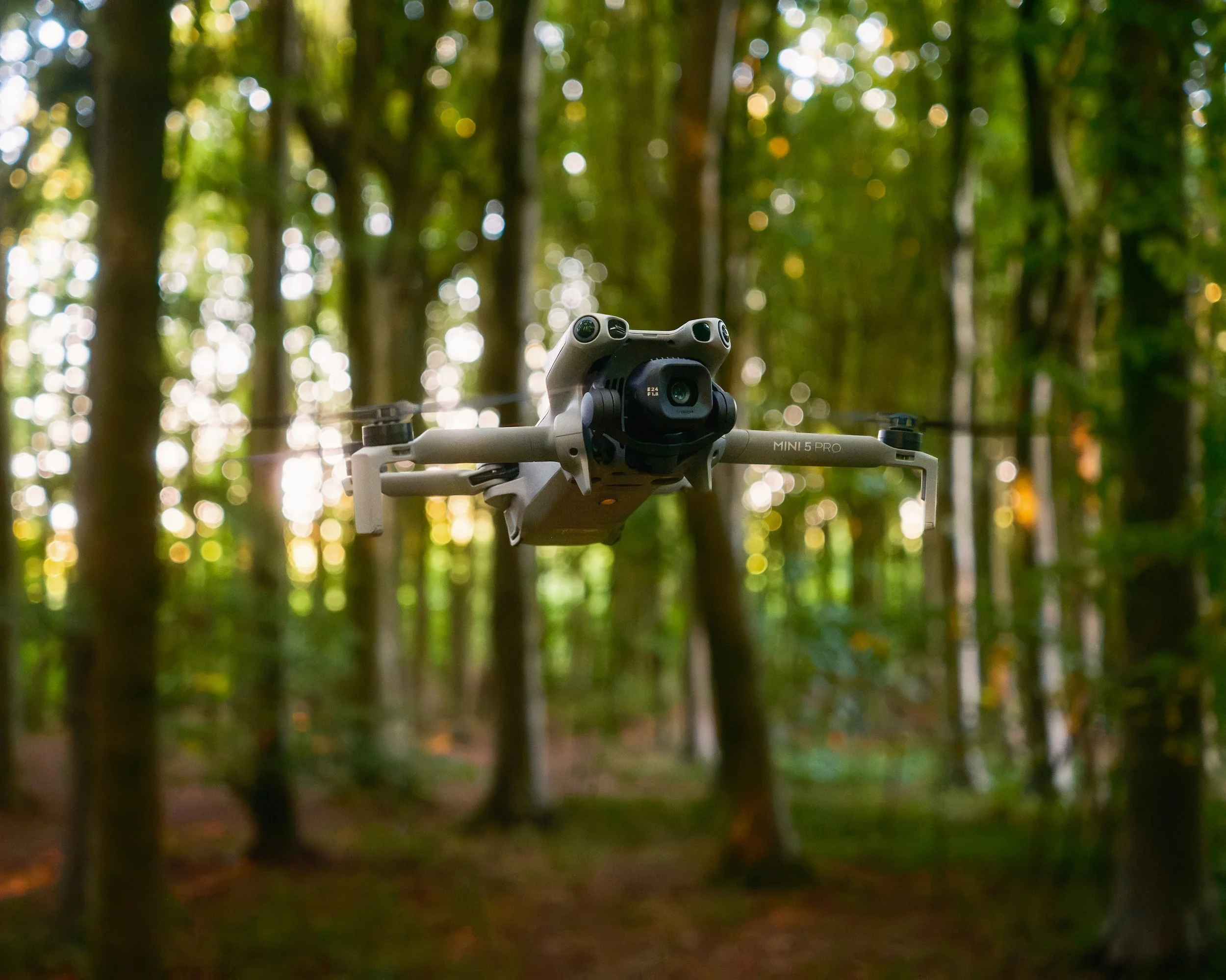 A drone flying through a wooded area with trees and sunlight in the background.
