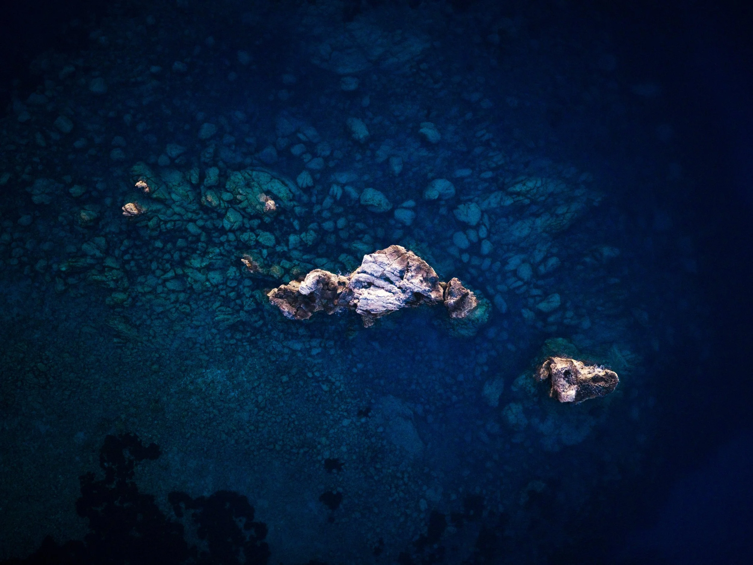Aerial view of rocky coastline with clear, dark blue water and scattered rocks