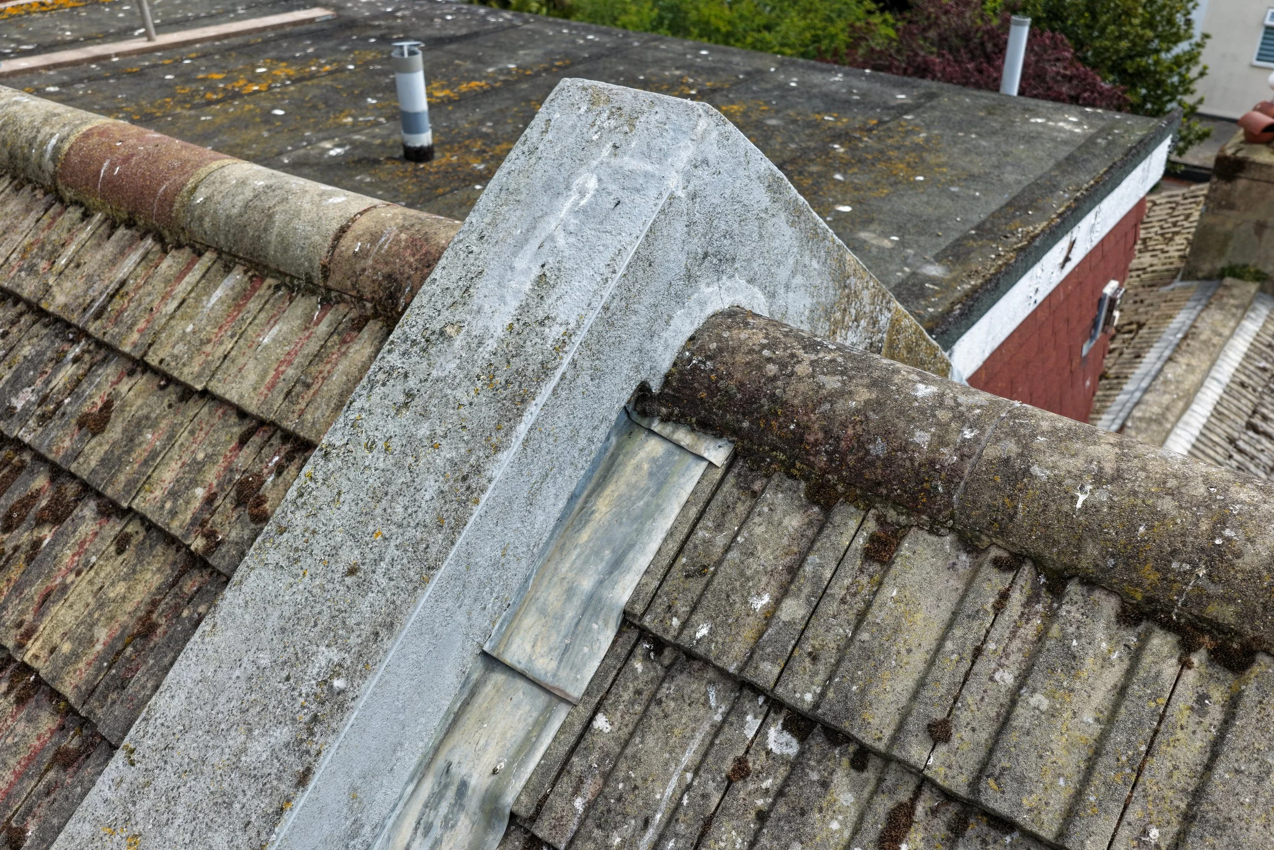 Close-up of a rooftop with aged, moss-covered tiles and weathered stone chimney cap.