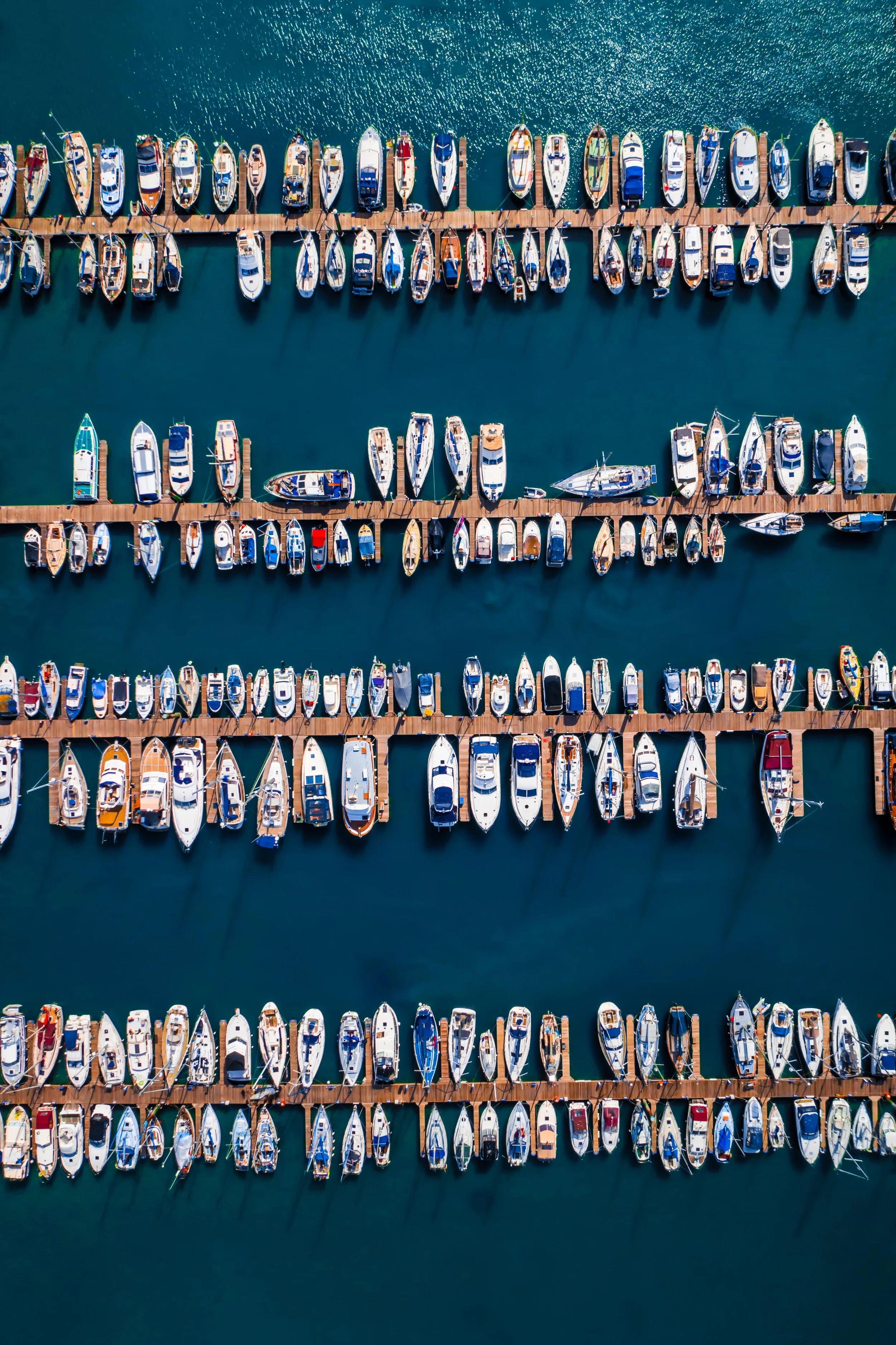 Aerial view of multiple boats docked at a marina with a wooden pier in the water.