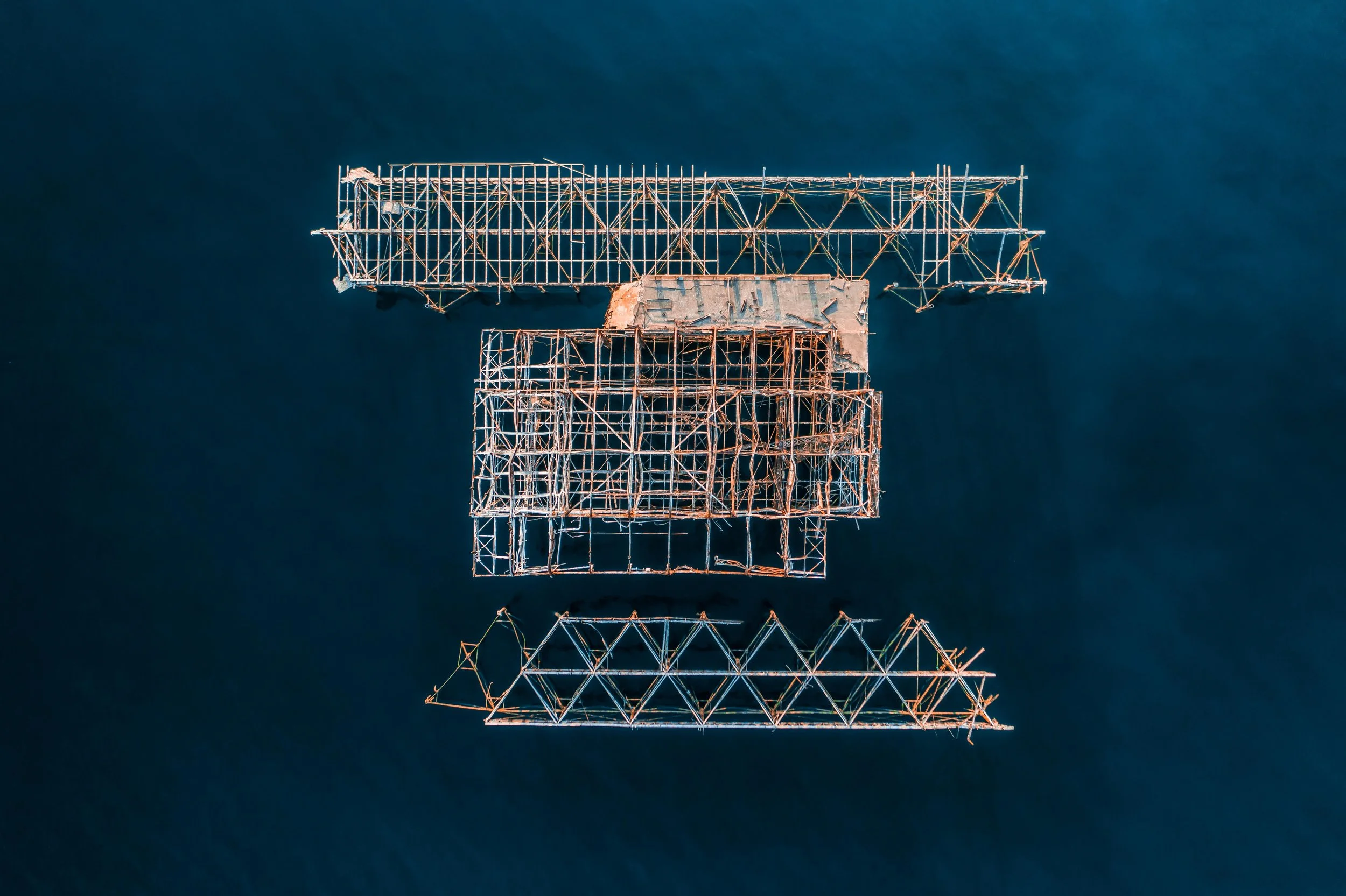 Top-down aerial view of Brighton West Pier, a tall, rusted industrial tower with a lattice structure, reflected in a dark body of water below.