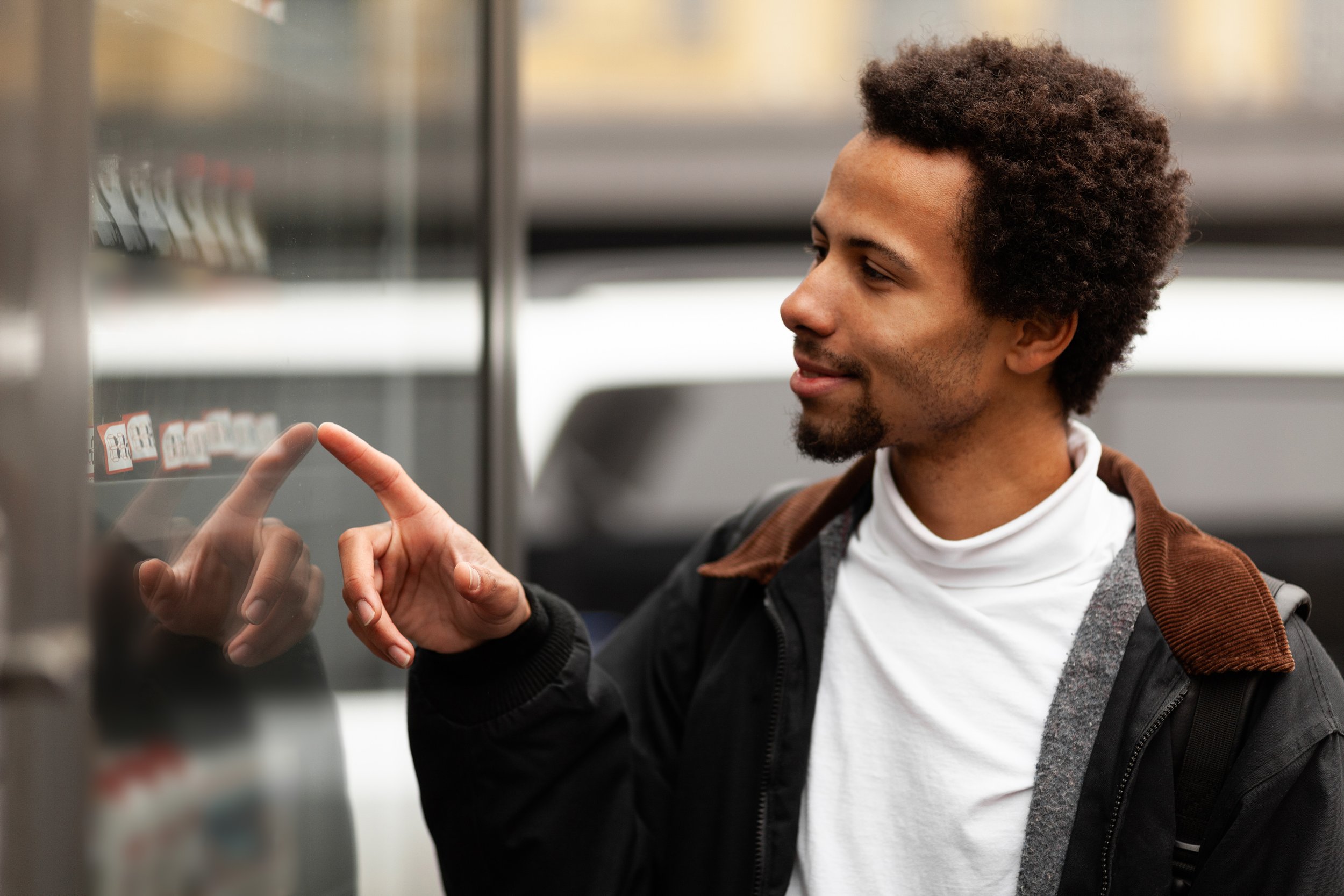 A young man with curly hair and a backpack using a touchscreen vending machine.