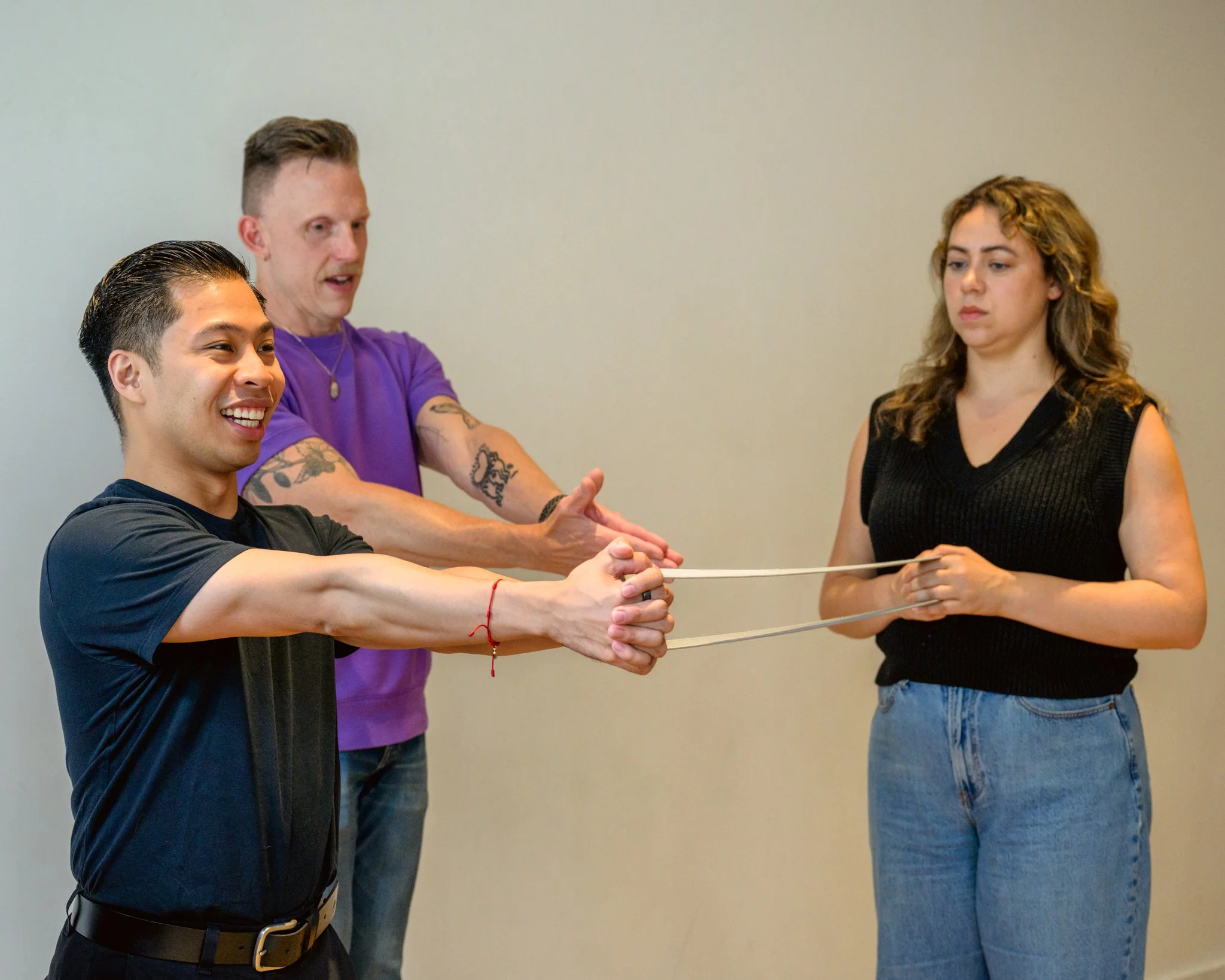Jaryd performs a Pallof Press, pressing a band in front of him as Tatiana holds the other end of the band and David demonstrates the press off to the side.