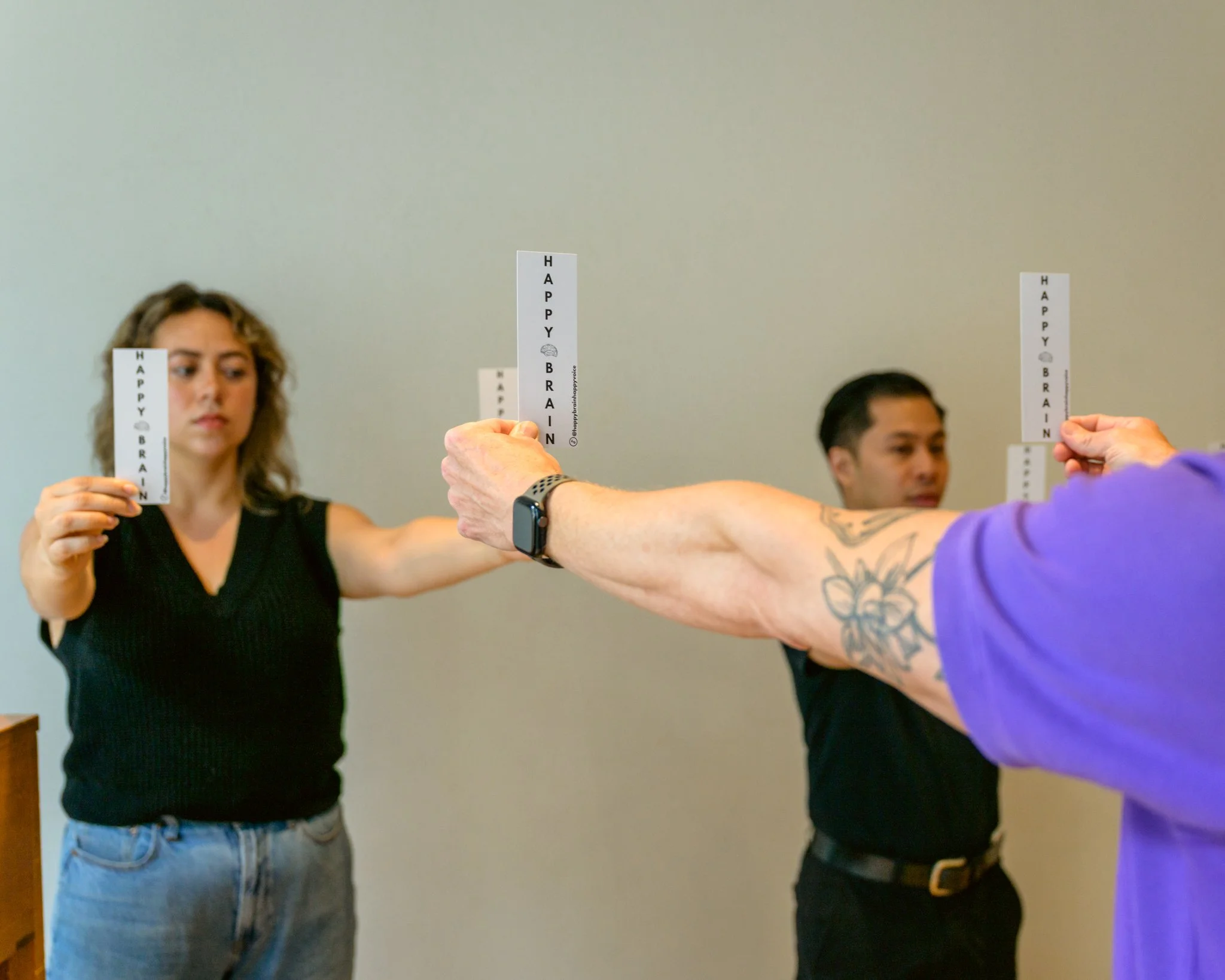 David, Jaryd, and Tatiana each hold 2 bookmarks at arm's length. The bookmarks say "Happy Brain"