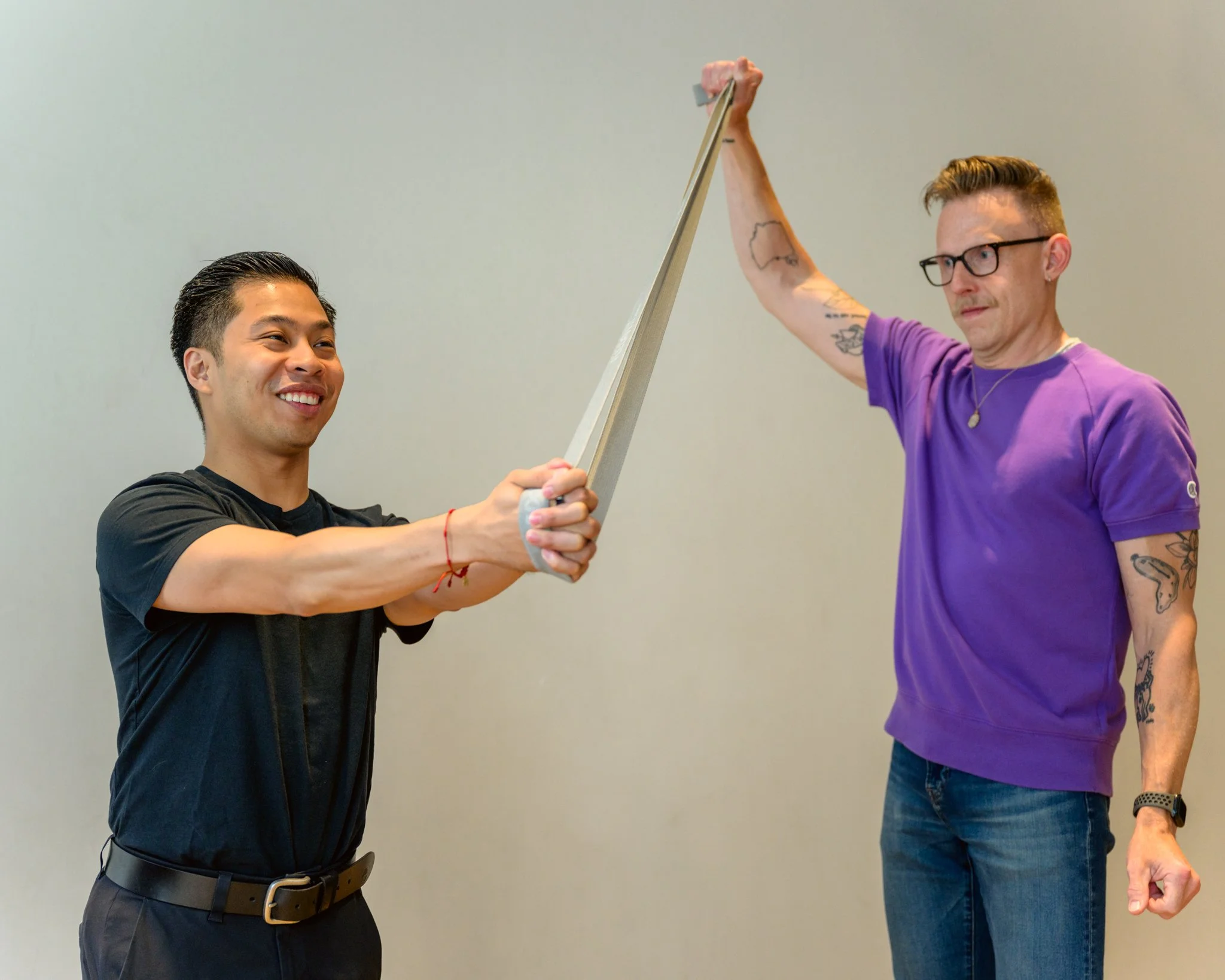 David holds a band up left of Jaryd, as Jaryd performs a Pallof Press, pressing the band out in front of him.