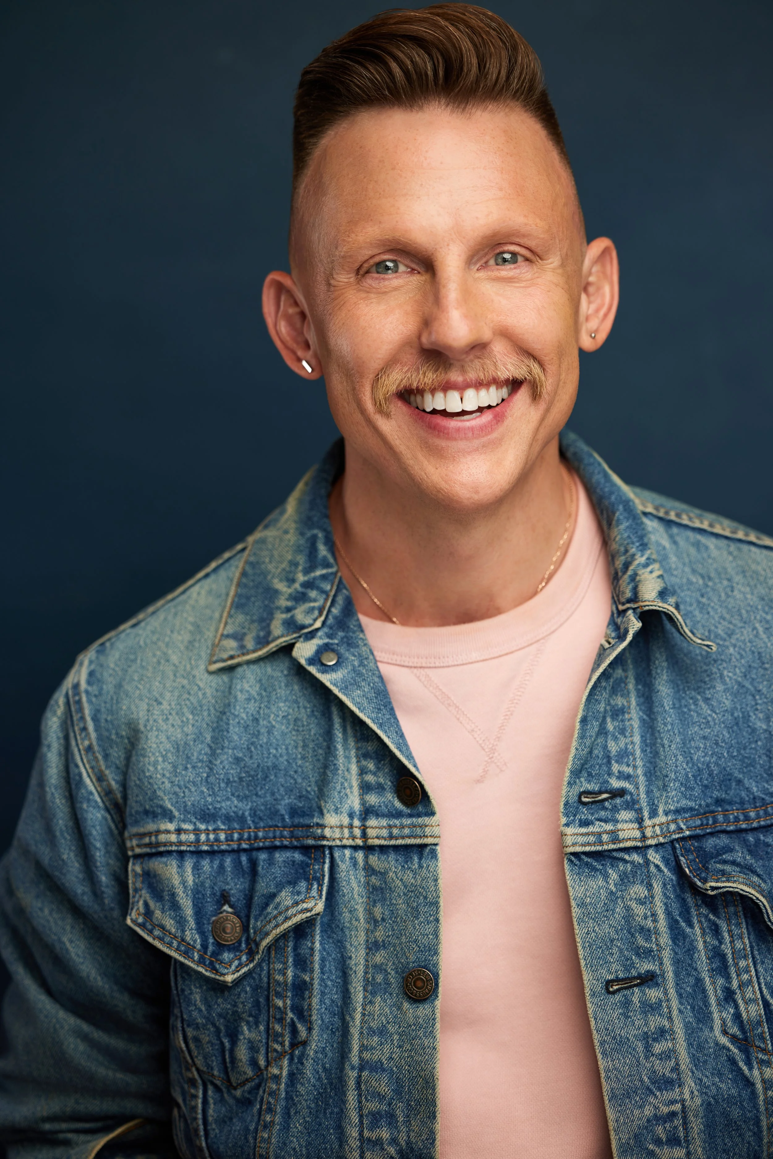 David, smiling, wearing a pink sweatshirt under a denim jacket