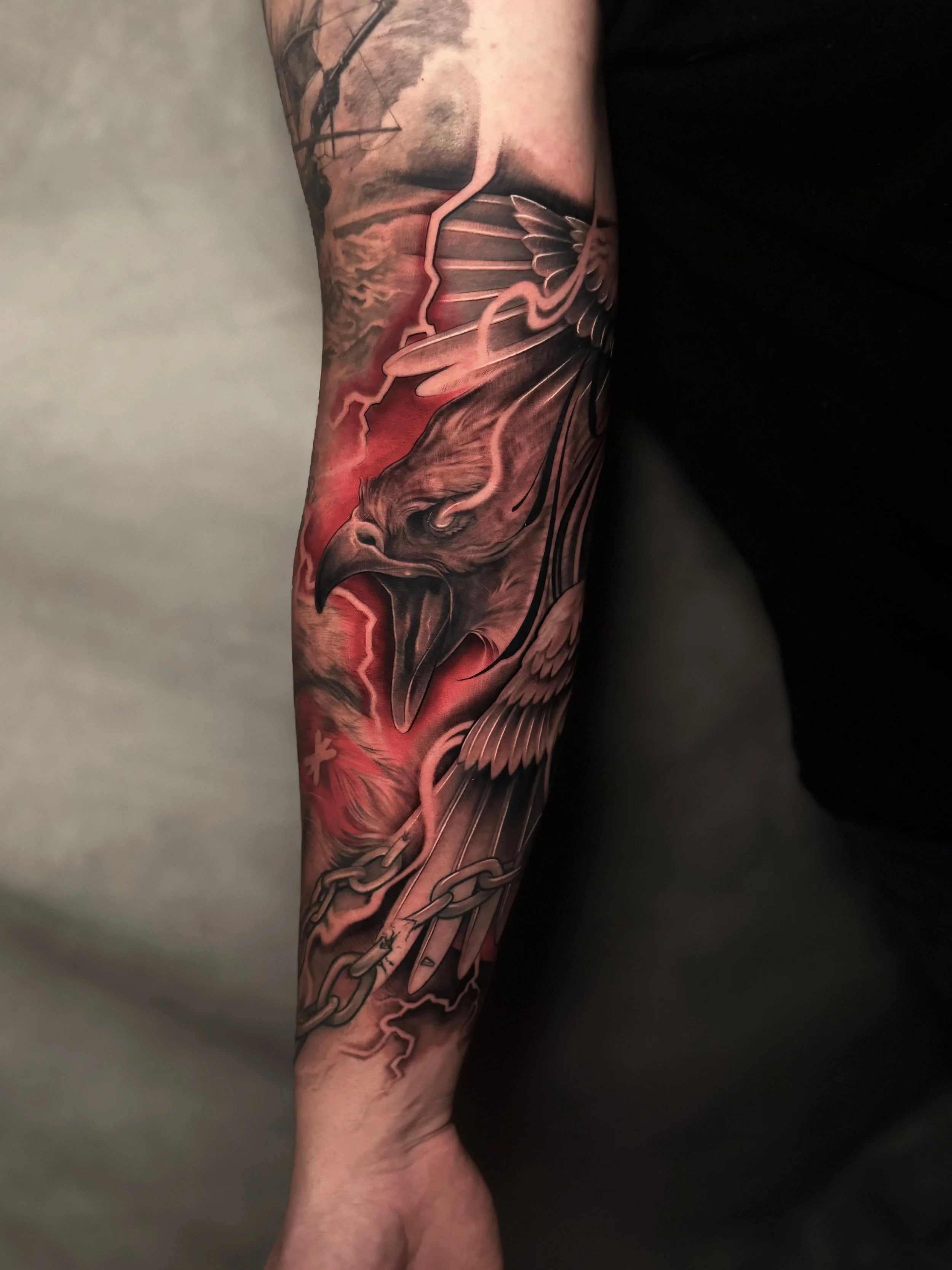 Tattoo of an eagle with a fierce expression, wings spread, surrounded by chains and lightning, with a red and black smoky background.