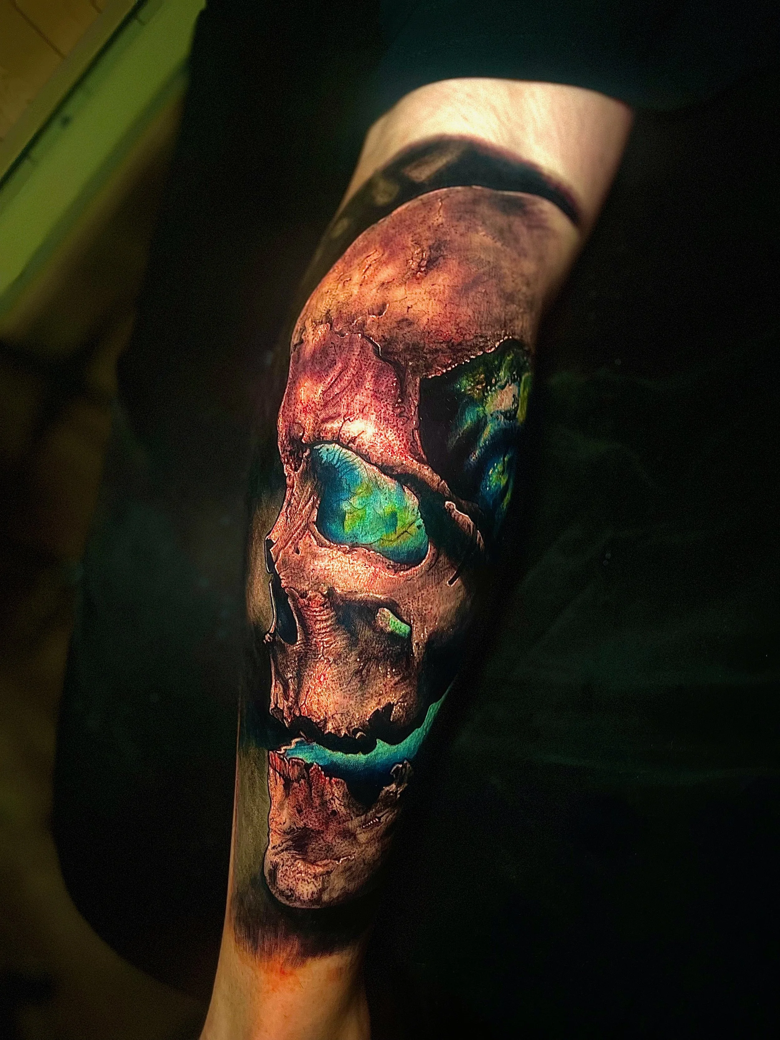 A realistic tattoo of a human skull with vibrant colors, including blues, greens, and reds, covering a person's arm.