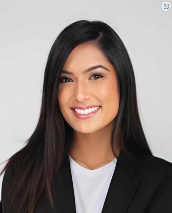 A young woman with long black hair smiling, wearing a black blazer and white shirt against a plain light gray background.