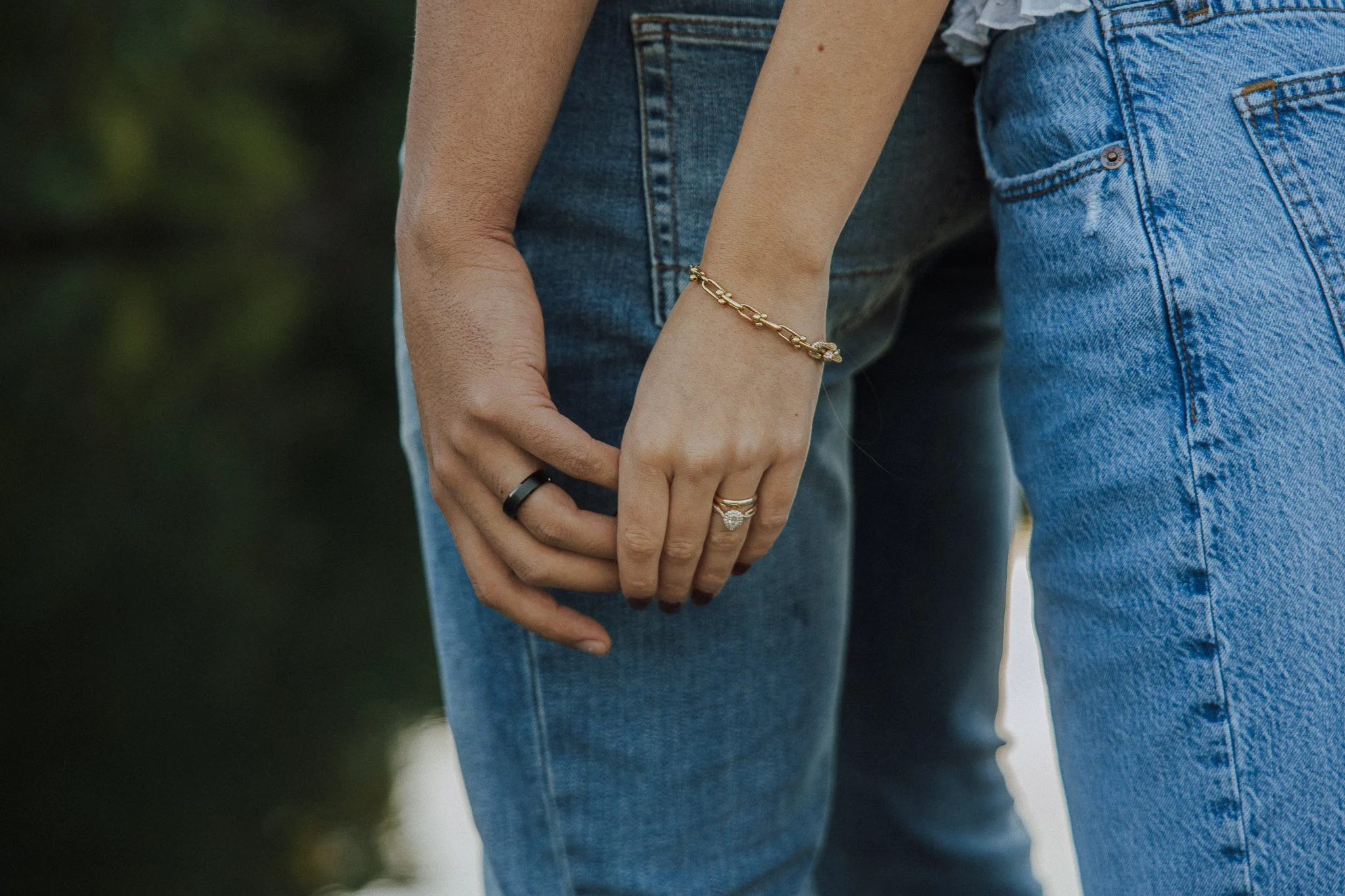 Close-up of a couple holding hands, showing their rings and jewelry, wearing blue jeans.