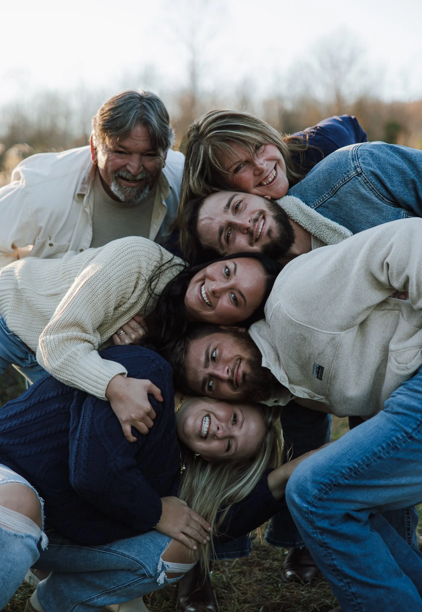 A group of people lying on the ground outdoors in a pile, smiling and having fun.