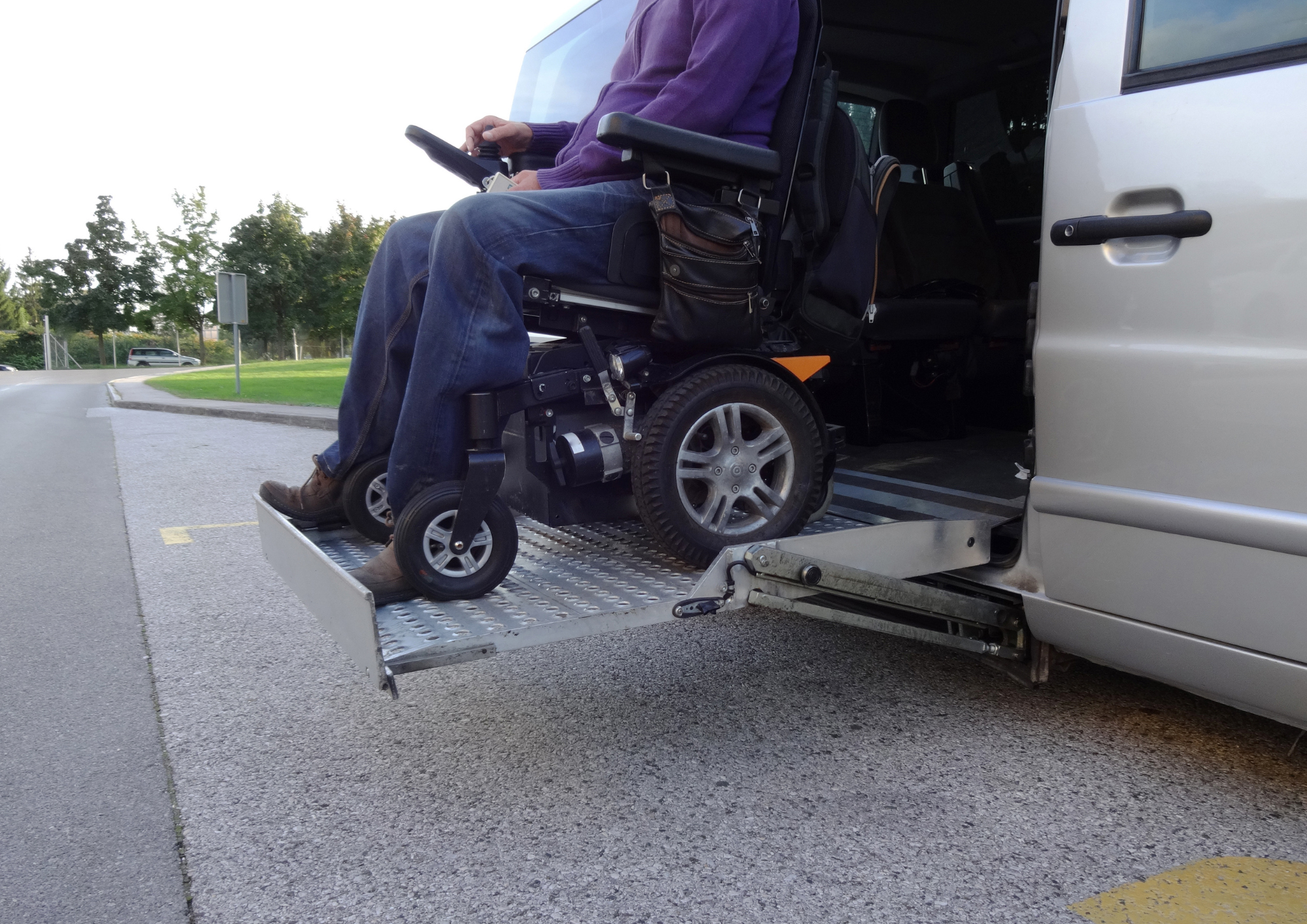 Individual in a purple shirt and jeans using a wheelchair lift to get into a van.