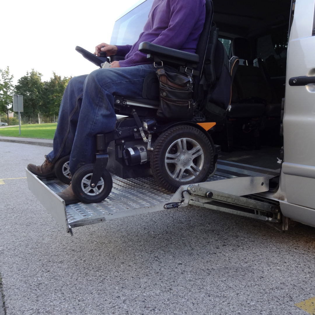 A person in a purple sweater and jeans sitting in a motorized wheelchair being lowered into a vehicle with a wheelchair accessible lift.