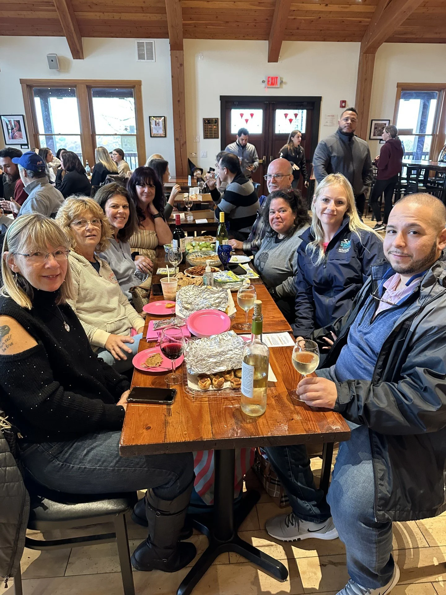 A group of people sitting around a wooden table having a meal in a restaurant, with some wine and food on the table.