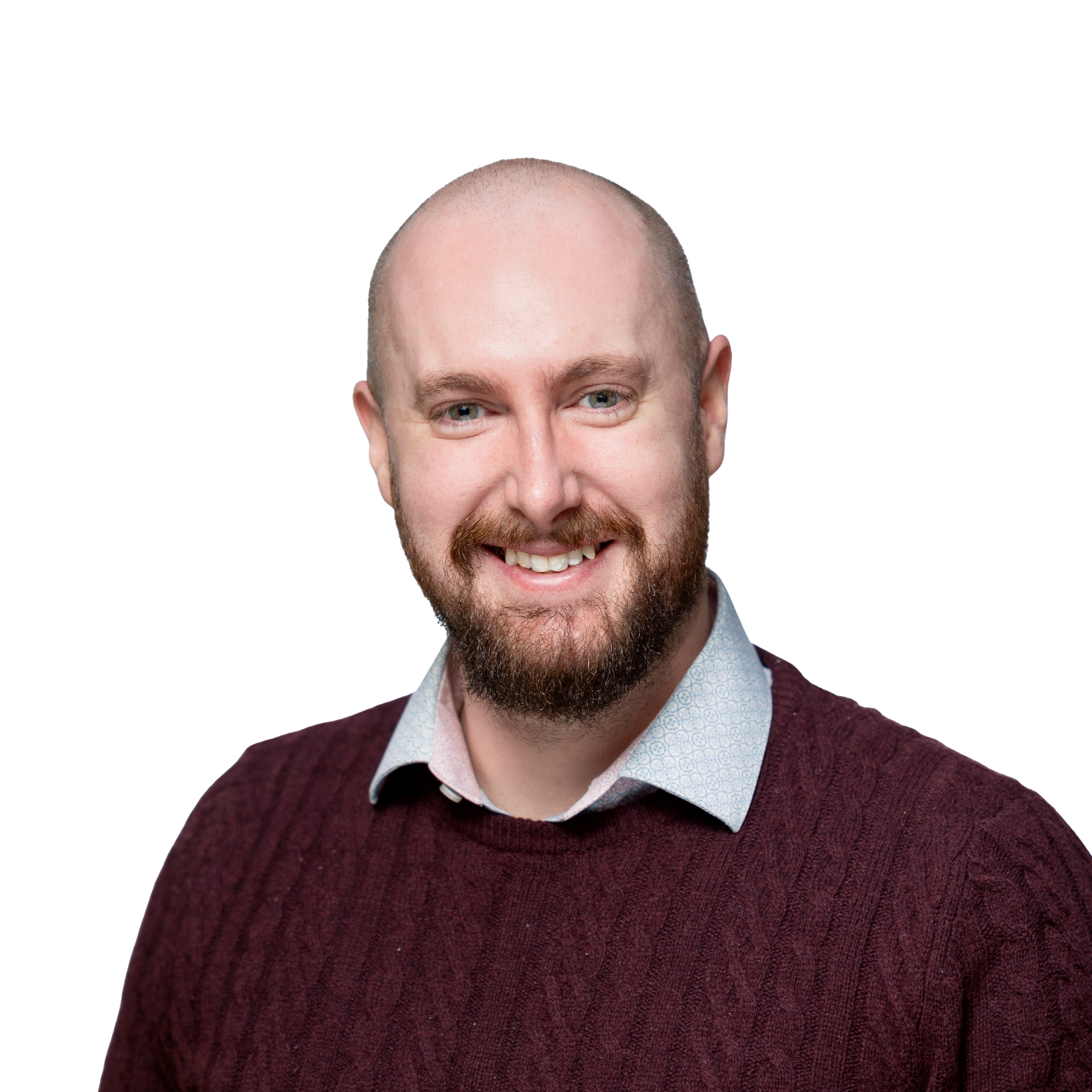 A smiling man with a beard and a shaved head, wearing a white collared shirt under a maroon cable-knit sweater, studio portrait against a black background.