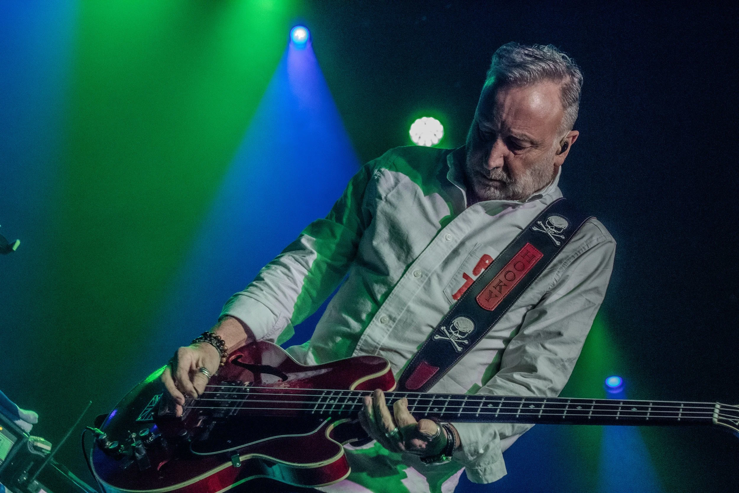 A man playing a bass guitar on stage with colorful green, blue, and purple lights.