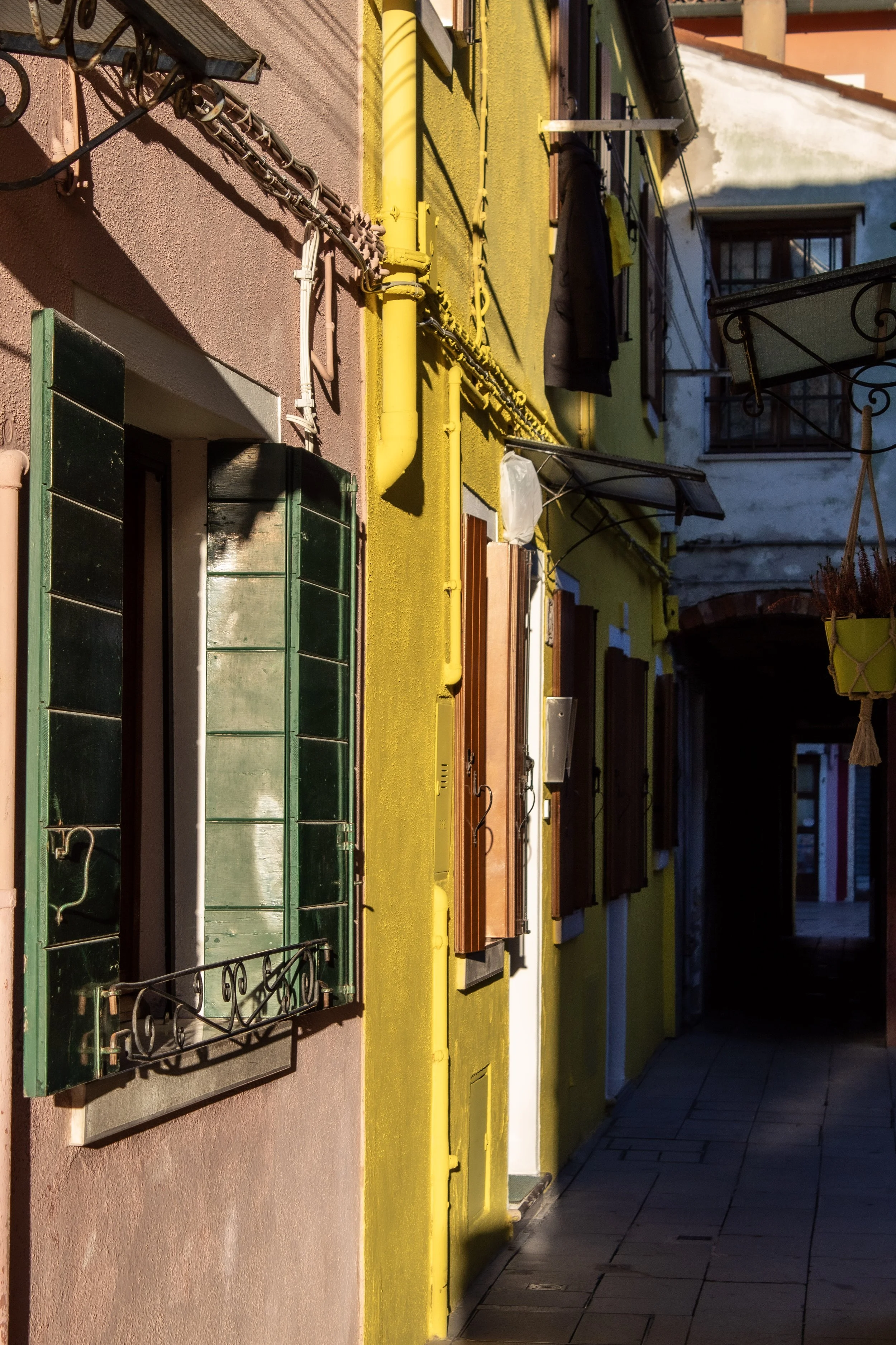 Colorful street with pink and yellow buildings, open window shutters, hanging laundry, and potted plants.
